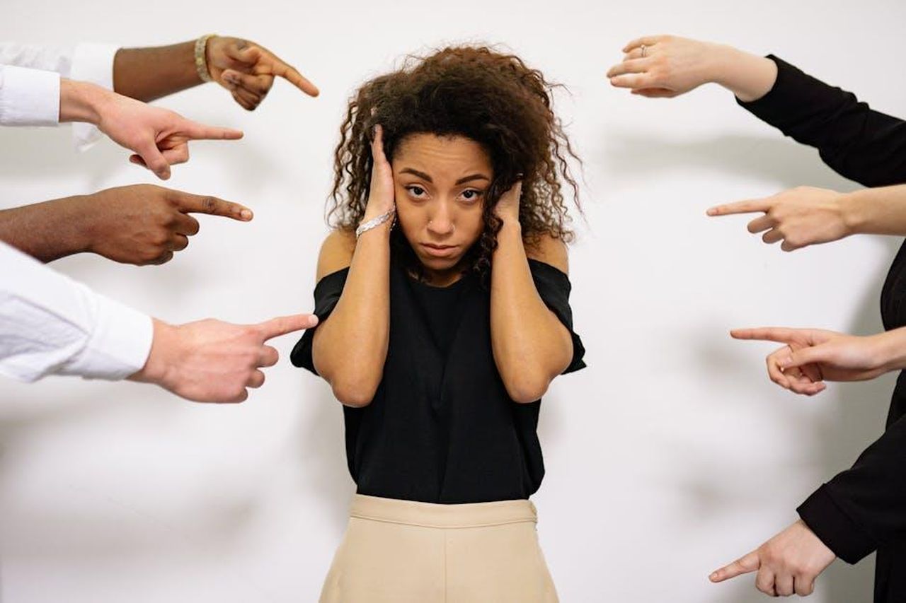 Le_accuse_contro_JayZ_e_Sean_Combs_cRZVUvb0lF - Confidenze24 Source: Yan Krukau - pexels - Stressed woman with hands on ears surrounded by pointing fingers, illustrating pressure.