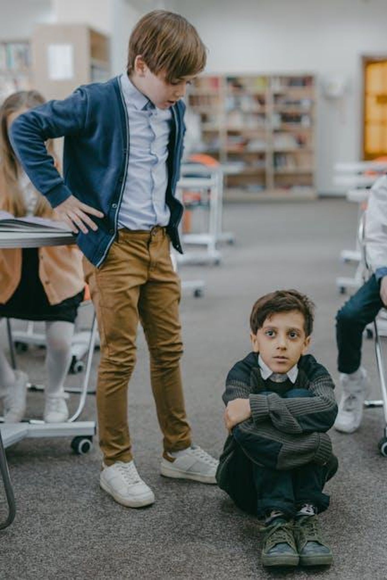 Le_accuse_di_molestie_e_bullismo_HL5f75LcQi - Confidenze24 Source: Mikhail Nilov - pexels - Two boys in a school library scene depicting a bullying incident, highlighting peer conflicts.
