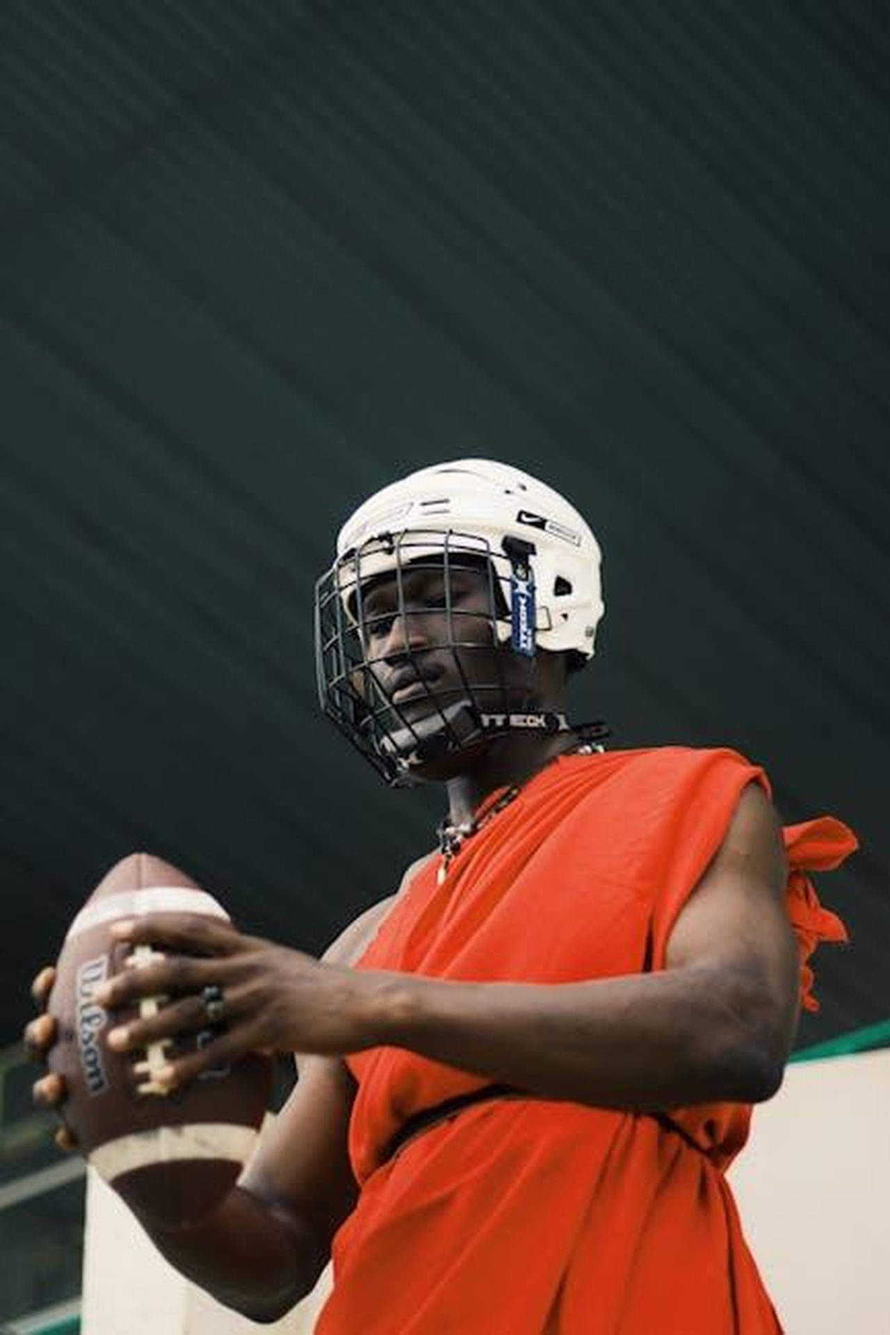 Le_accuse_e_la_difesa_di_Alaila_Everett_F5aSTky9De - Confidenze24 Source: Tim Yisa - pexels - African athlete in traditional attire with helmet and football, blending cultures.
