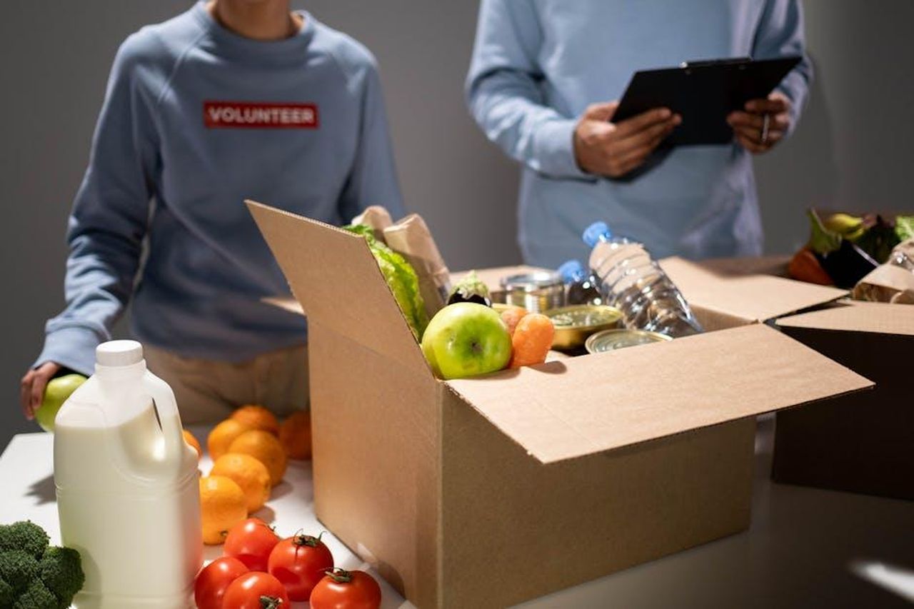 Le_attivit_benefiche_di_Kate_rispetto_a_Meghan_5QBpWBGERl - Confidenze24 Source: cottonbro studio - pexels - People packing a cardboard box with essentials like fruits, vegetables, and bottled water for charity.