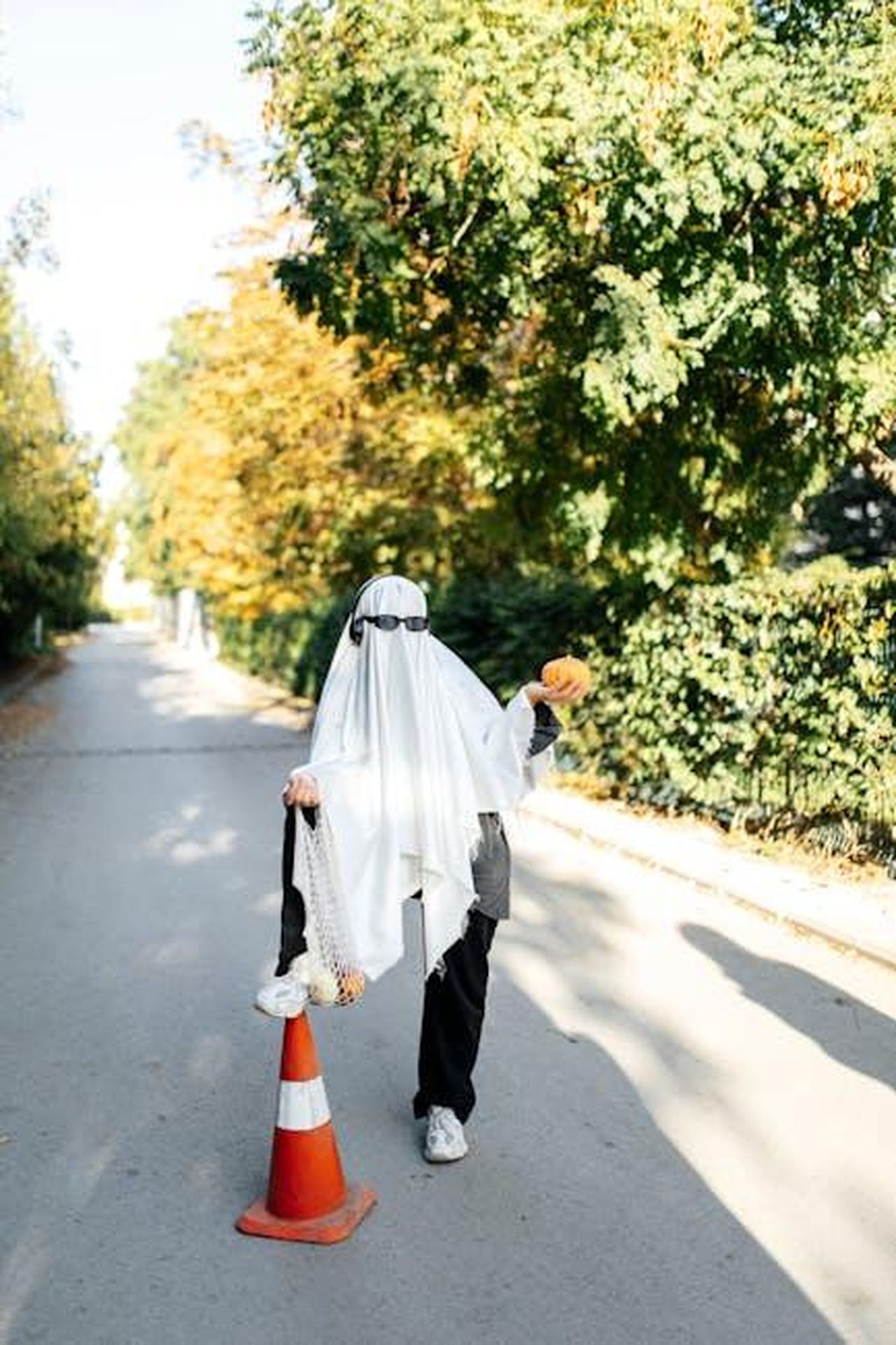 Le_battute_di_Ben_Affleck_sulla_cotta_di_Lopez_YRgHCJ0To0 - Confidenze24 Source: Esma Atak - pexels - A person in a ghost costume stands on a sunny city street, holding a pumpkin, showcasing urban Halloween spirit.