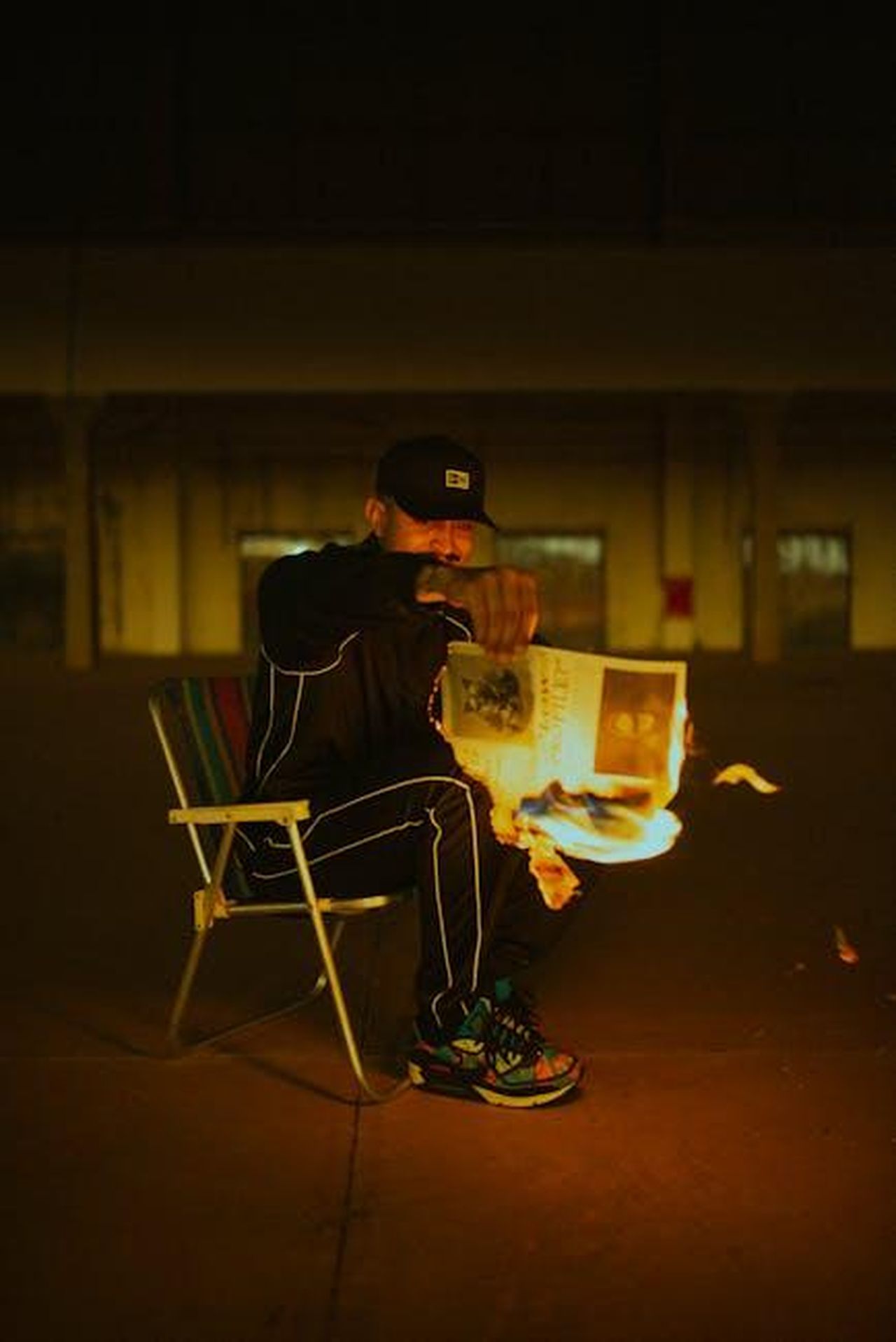 Le_conseguenze_del_commento_di_Smith_33kQZOdpC4 - Confidenze24 Source: Isabella Mendes - pexels - A man in sports clothing holds a burning newspaper while sitting on a chair indoors.