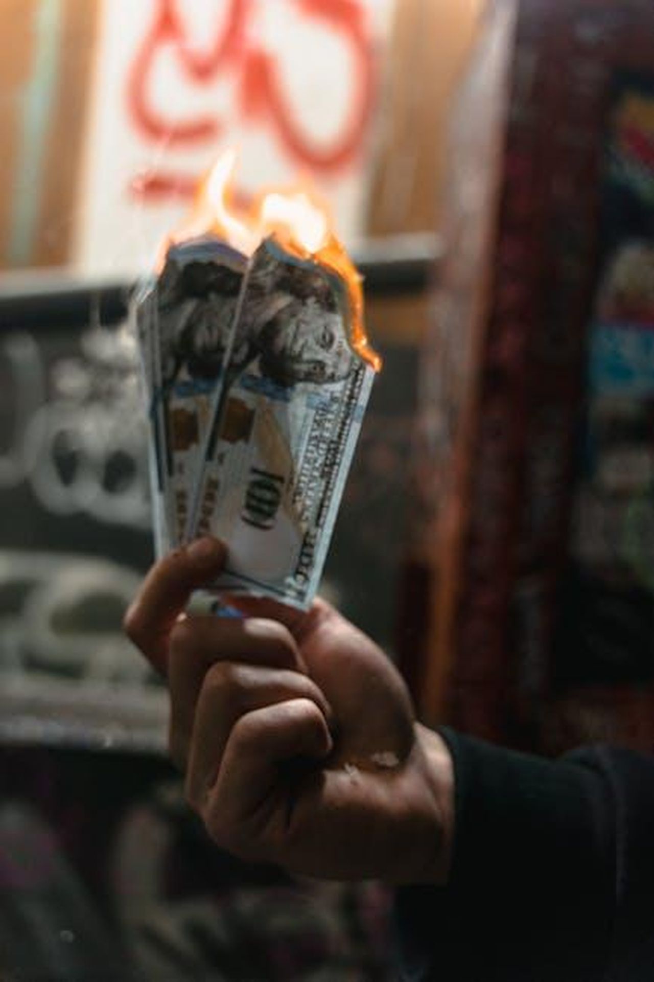 Le_conseguenze_dellepidemia_di_morbillo_FvsIxF9Xfu - Confidenze24 Source: MART PRODUCTION - pexels - Dramatic image of burning dollar bills held against a graffiti-covered wall, symbolizing waste.
