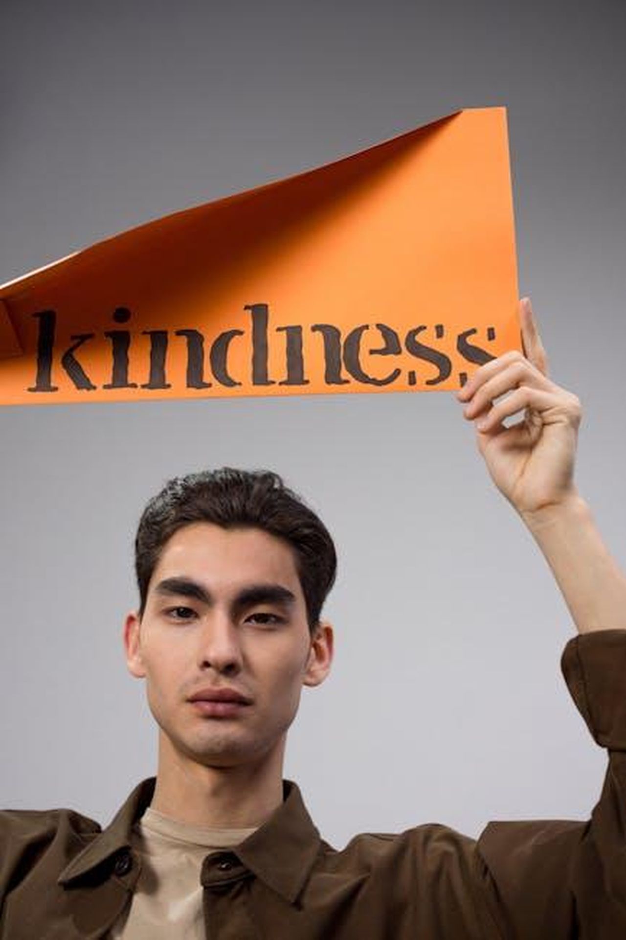 Le_dichiarazioni_di_Chandauka_e_le_reazioni_2AEWDbijh1 - Confidenze24 Source: Ron Lach - pexels - Man holds orange paper sign with 'kindness' text, promoting positive message.