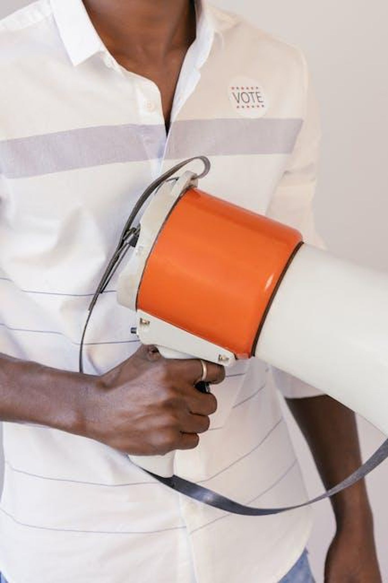 Le_differenze_politiche_e_la_rivalit_ybexgU6H3a - Confidenze24 Source: Mikhail Nilov - pexels - Close-up of a person holding a megaphone, promoting voting awareness, with a 'Vote' sticker on the shirt.