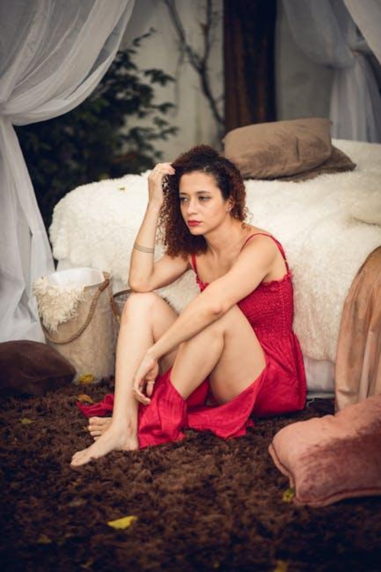 Le_emozioni_di_Liev_Schreiber_sul_red_carpet_KdlxcOWQod - Confidenze24 Source: Leticia Gonsalli - pexels - Thoughtful woman in red dress on brown rug beside a bed, indoors.