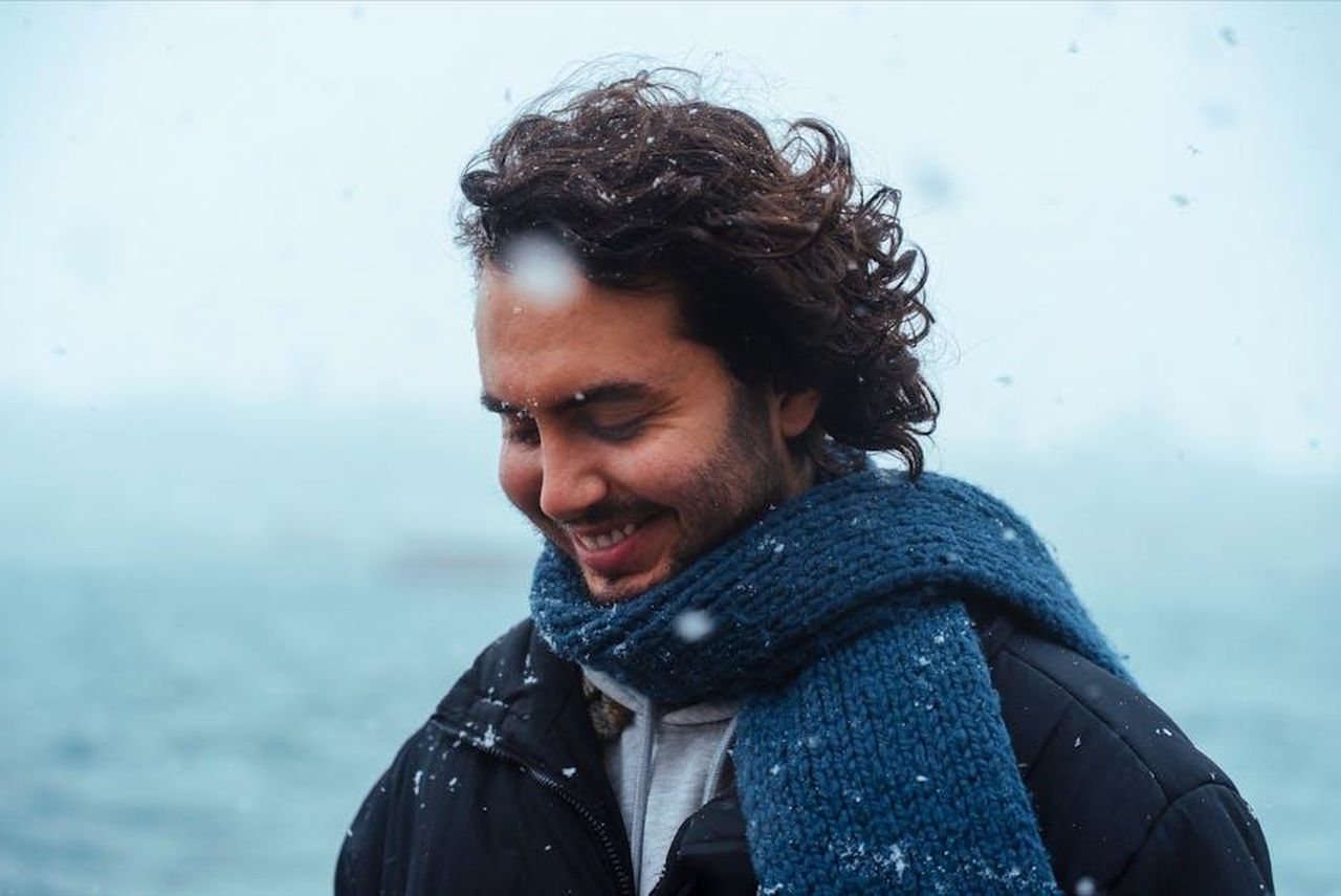 Le_emozioni_di_Mikey_dopo_la_vittoria_dByt99HPC9 - Confidenze24 Source: Harun - pexels - Man with curly hair in a scarf smiling in a snowstorm near the sea.
