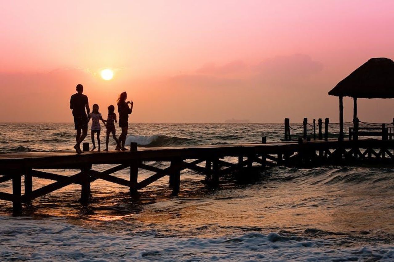 Source: Pixabay - pexels - Silhouetted family enjoys a stroll on the beach pier at a vibrant sunset over the ocean waves.