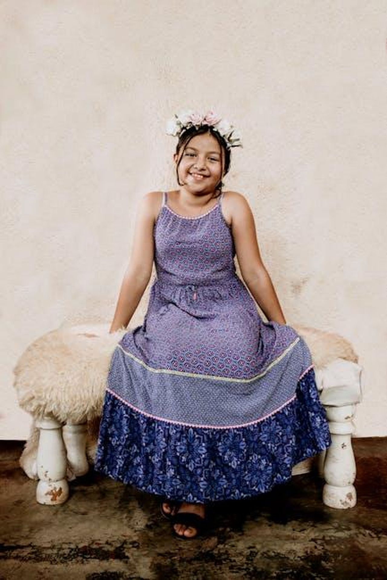 Le_figlie_di_Serena_come_modelle_hT9P7vW0rL - Confidenze24 Source: Giezi suhul Gonzalez - pexels - A young girl wearing a blue dress and flower crown, sitting happily on a bench indoors.