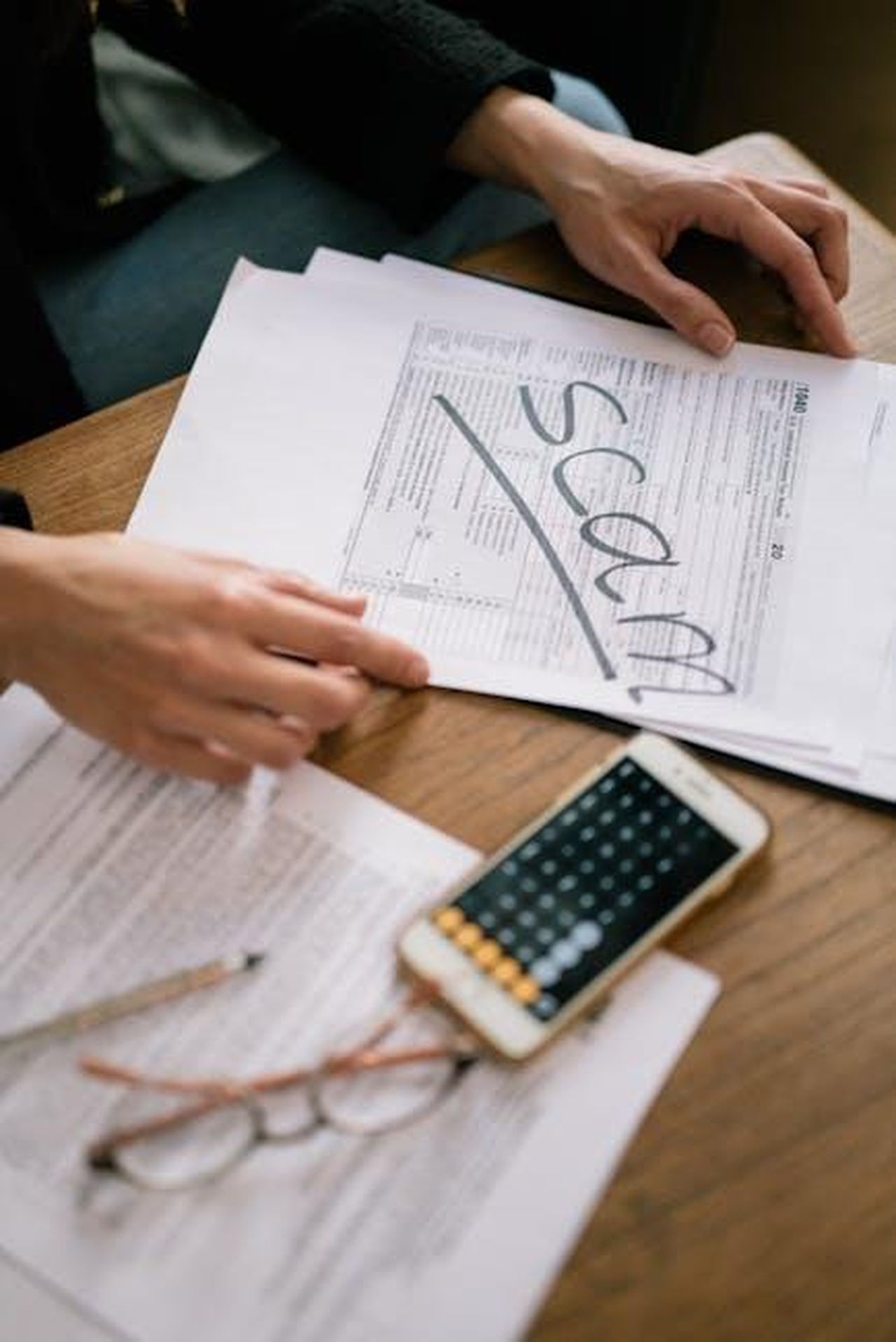 Le_lamentele_si_accumulano_qX6ctaObgD - Confidenze24 Source: Leeloo The First - pexels - Close-up of hands examining documents marked 'scam' with a calculator nearby.