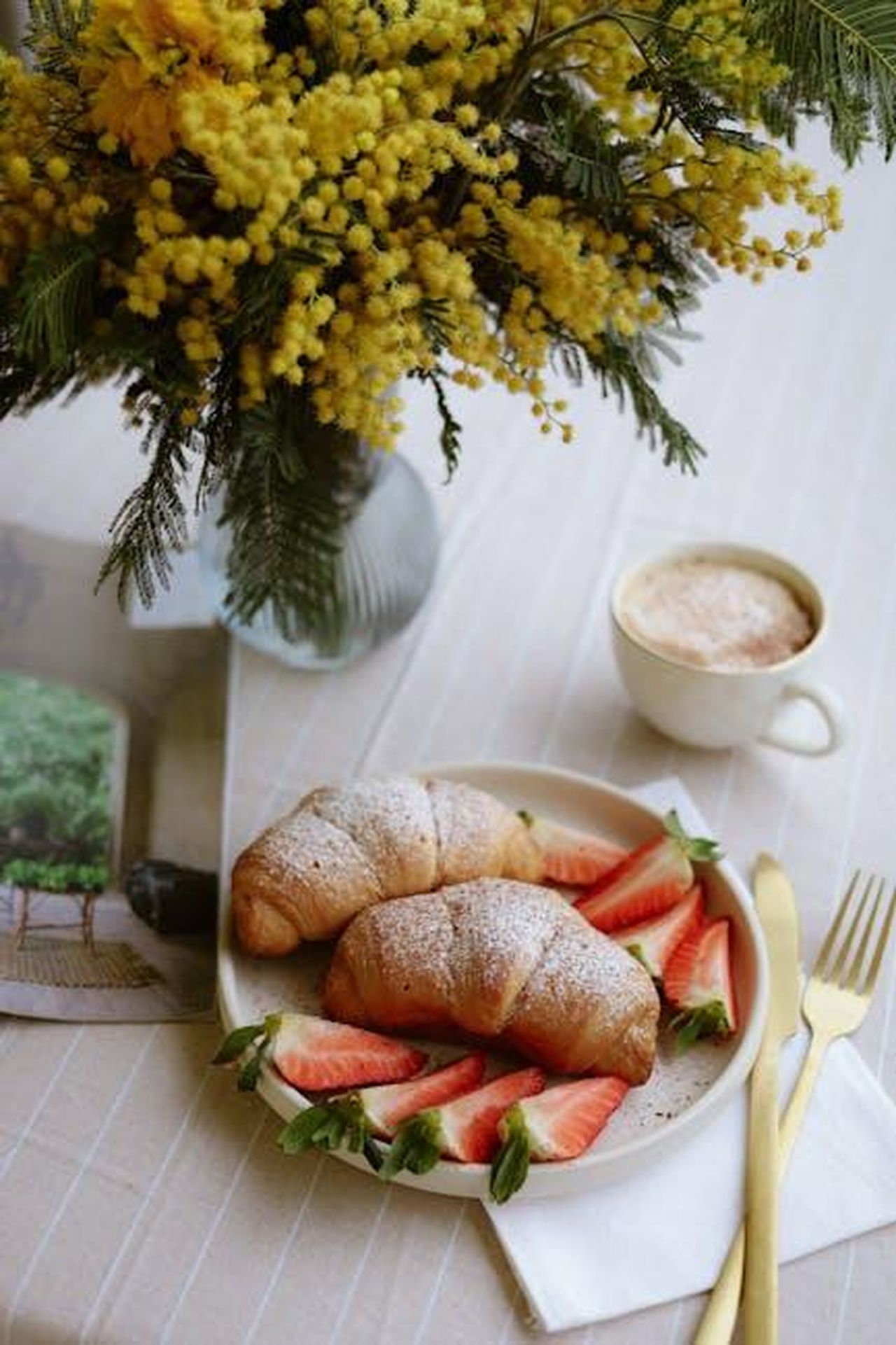 Le_paure_di_avvelenamento_delle_bevande_Sa8SmIszOJ - Confidenze24 Source: Nati - pexels - Elegant breakfast setup with croissants, strawberries, cappuccino, and floral decor.
