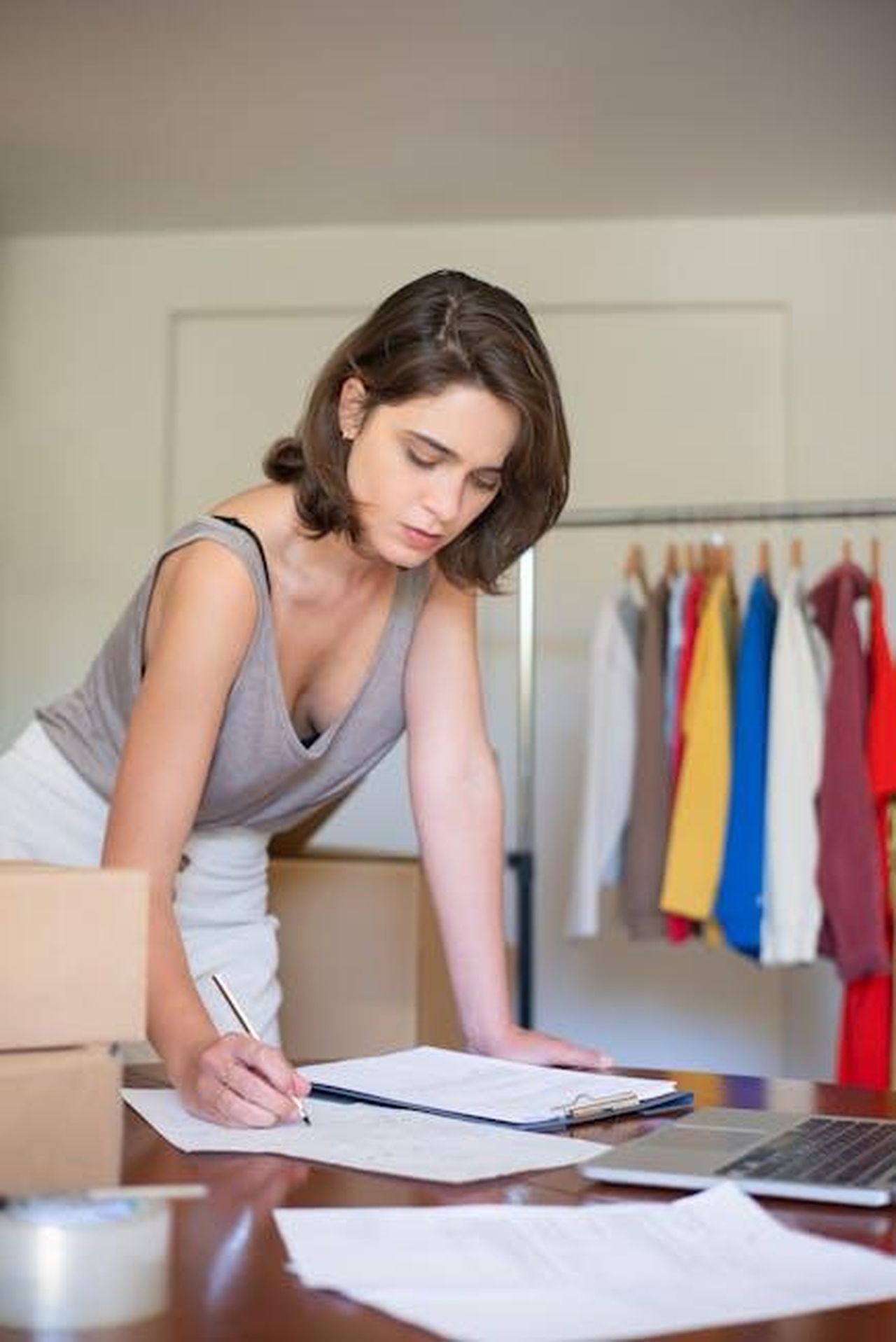 Le_ragioni_dietro_luscita_di_Donatella_da_Versace_iydS1FotR6 - Confidenze24 Source: Kampus Production - pexels - A young woman writes in her online store, surrounded by clothes and shipping boxes.