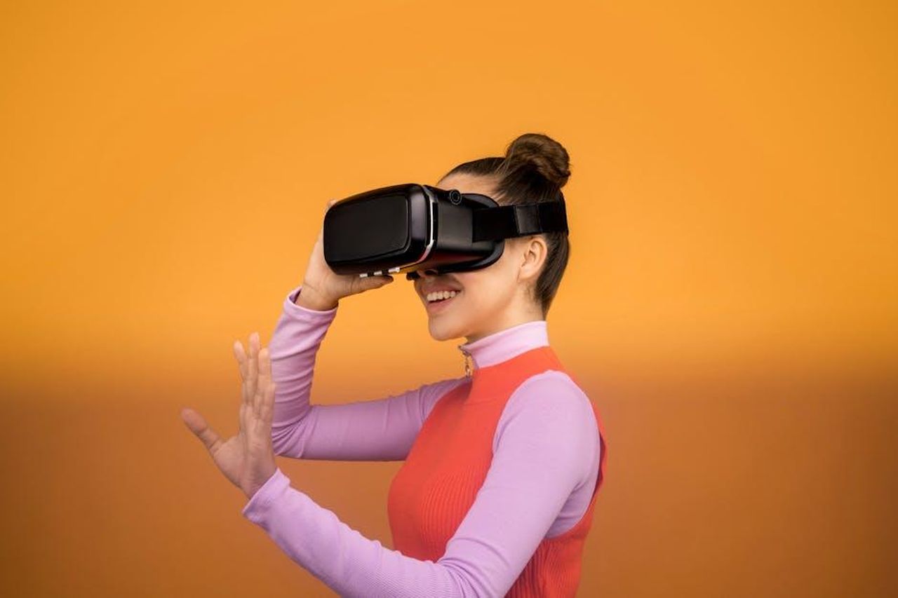 Le_reazioni_di_Megyn_Kelly_e_Don_Lemon_GnI9lc6grG - Confidenze24 Source: Sound On - pexels - A woman smiling and interacting with a VR headset against an orange background.
