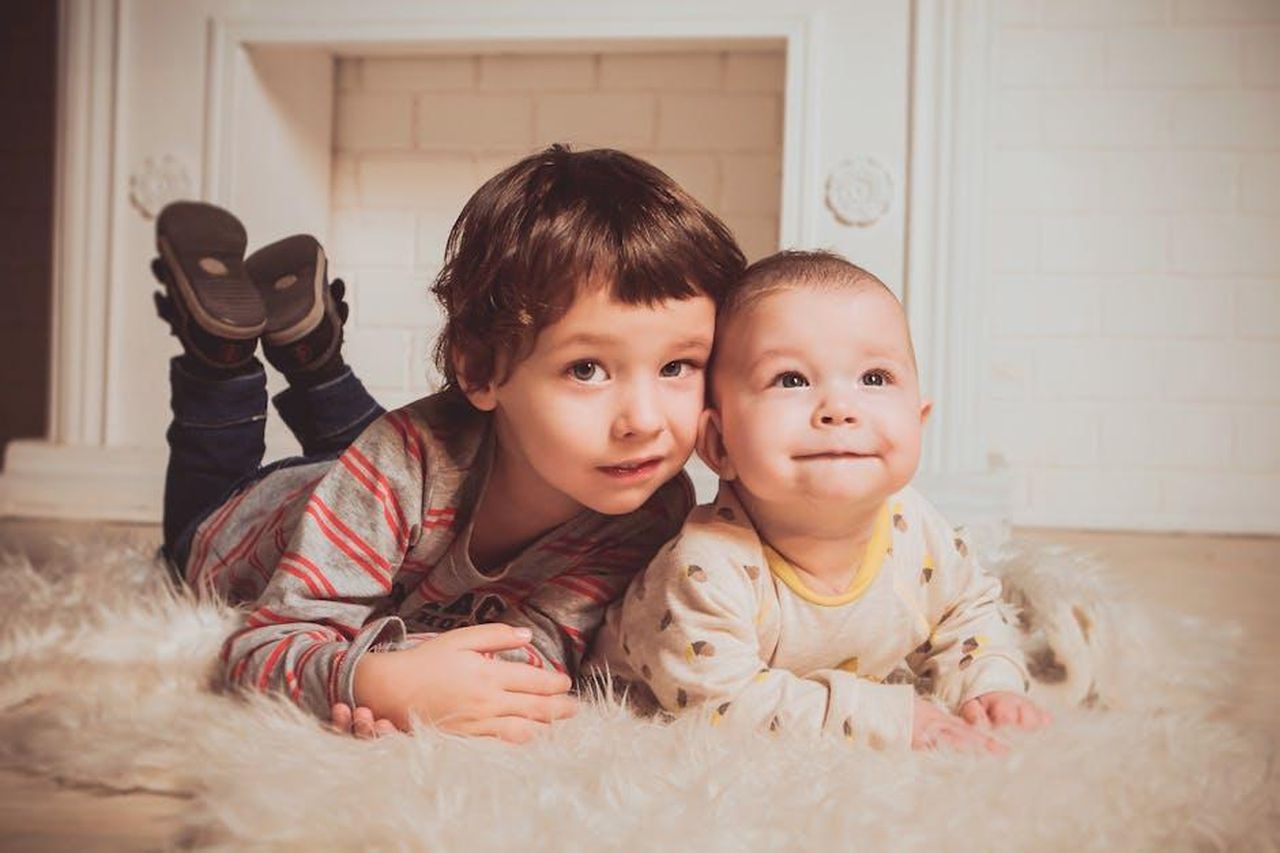 Le_rivelazioni_di_Vivian_sui_suoi_fratelli_UhbbHP7LkI - Confidenze24 Source: Vika Glitter - pexels - Two young siblings lying on a fluffy rug indoors, exemplifying warmth and family bonding.