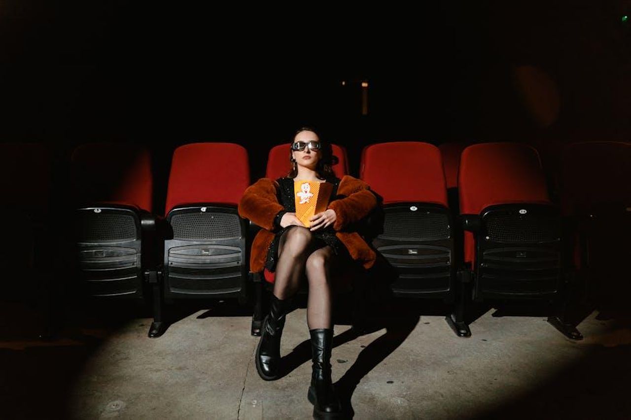 Le_sfide_al_box_office_tra_i_film_2Drv0le84F - Confidenze24 Source: Tima Miroshnichenko - pexels - A stylish woman sits alone in a dark cinema, enjoying popcorn during a movie.