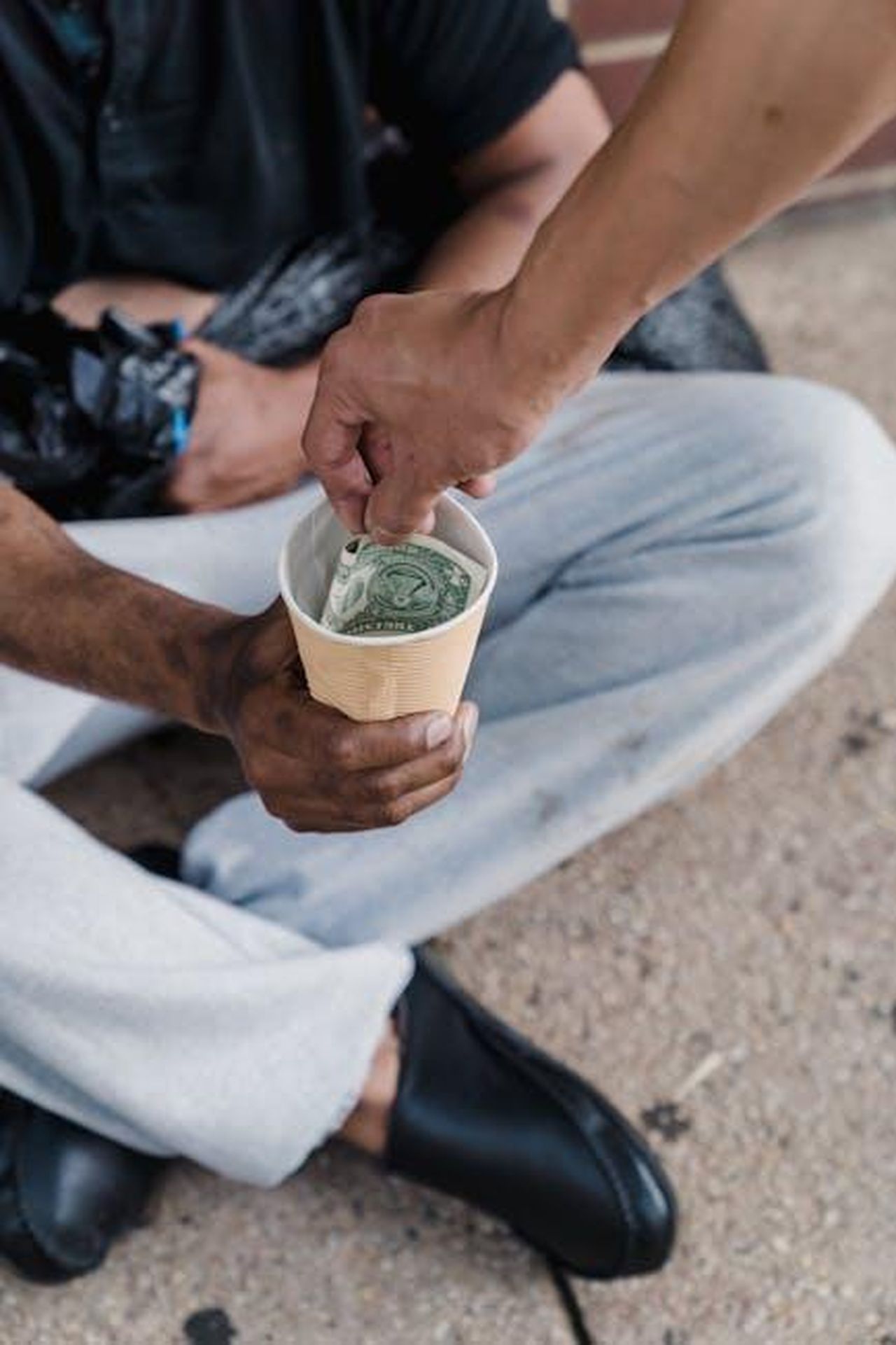 Le_sfide_del_lavoro_filantropico_M68AHGgcly - Confidenze24 Source: Timur Weber - pexels - Close-up of a person giving money to a beggar with a paper cup outdoors.
