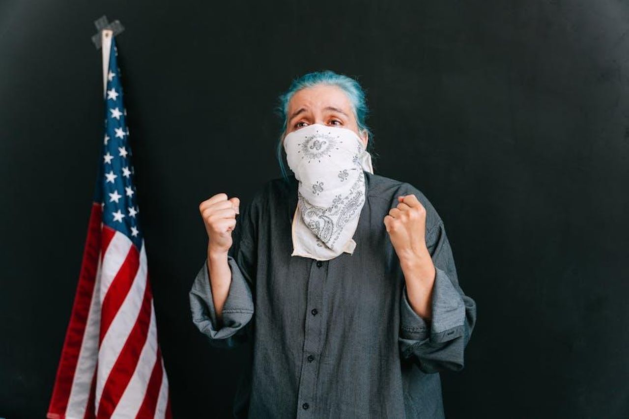 Le_tensioni_politiche_tra_Zegler_e_Gadot_WjVD5OvQLO - Confidenze24 Source: Ivan Samkov - pexels - A woman passionately protesting with clenched fists, wearing a bandana mask, next to an American flag.