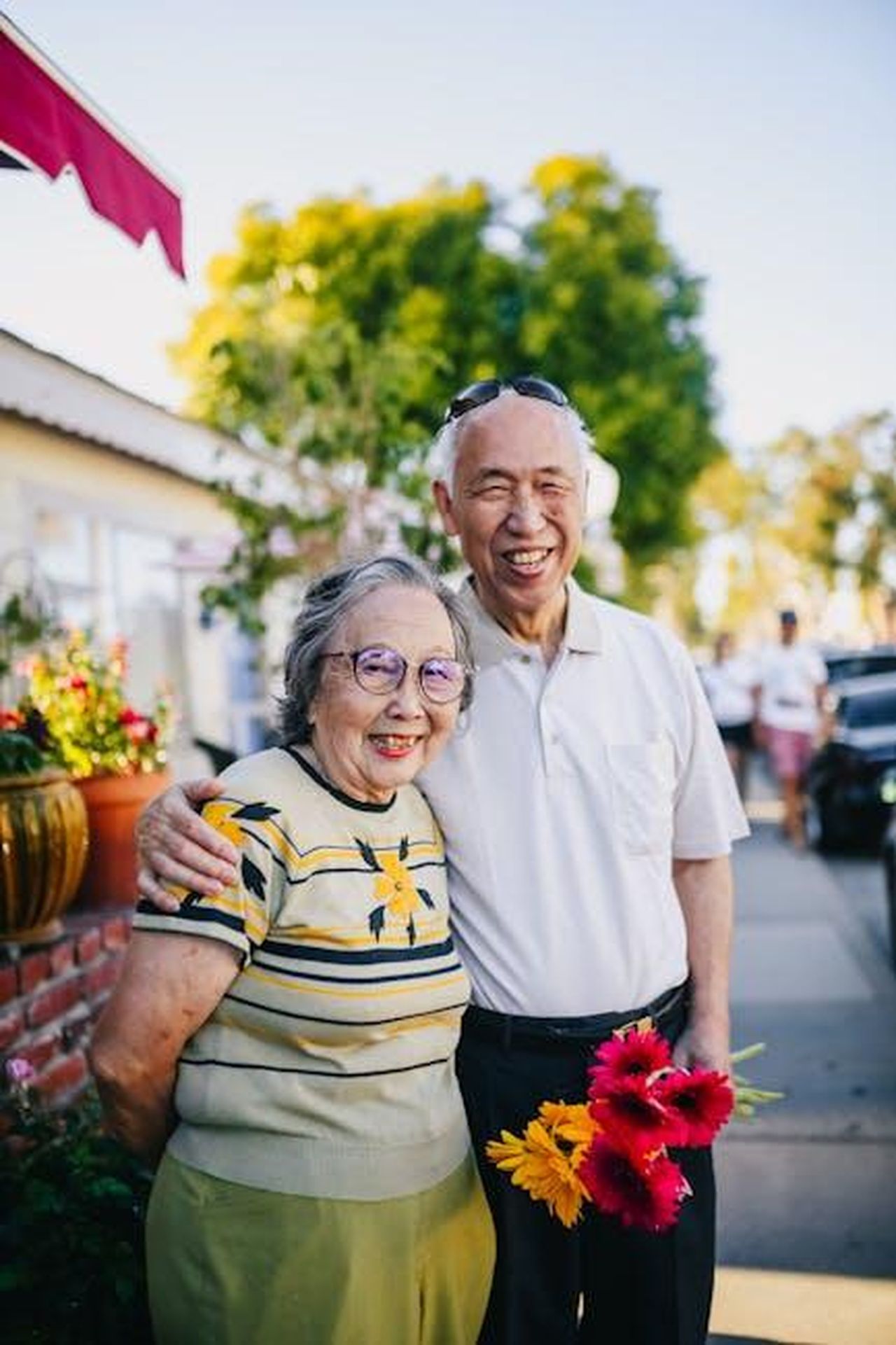 Le_testimonianze_della_famiglia_Franke_rwEULCqaJi - Confidenze24 Source: RDNE Stock project - pexels - A happy elderly couple embracing outdoors, holding flowers on a sunny day.