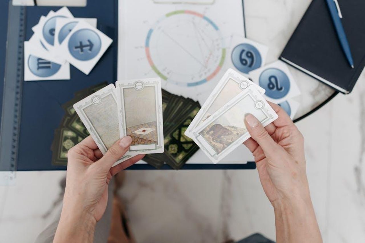 Leone_23_luglio__22_agosto_ybMCO2k1ej - Confidenze24 Source: Pavel Danilyuk - pexels - Hands holding tarot cards above an astrological chart with zodiac symbols scattered on the table.