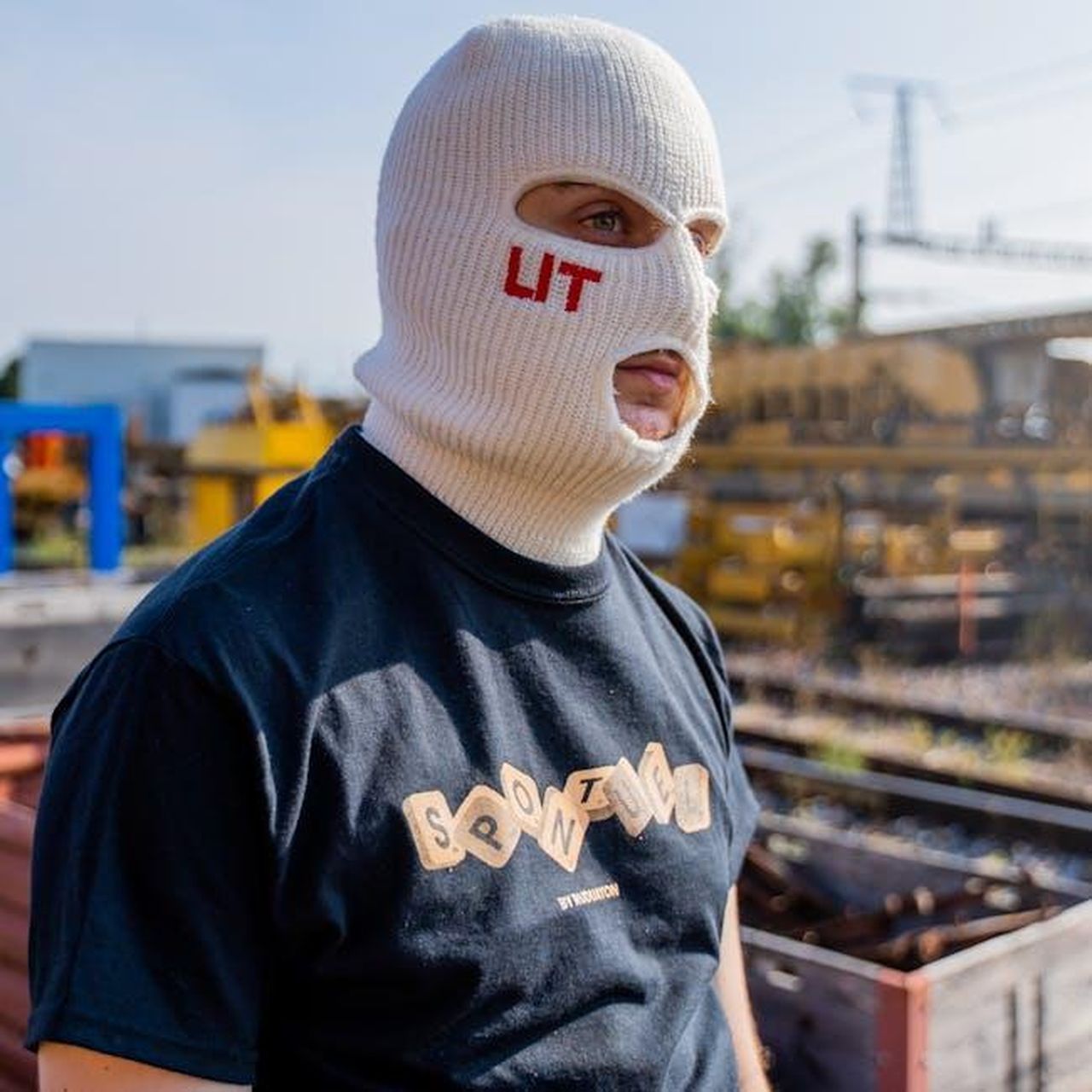 Limpatto_di_Meghan_sui_marchi_di_moda_V5cAFOJBRl - Confidenze24 Source: Evan Velez Saxer - pexels - A man in urban streetwear wearing a knit balaclava with 'LIT' text, posing outdoors.
