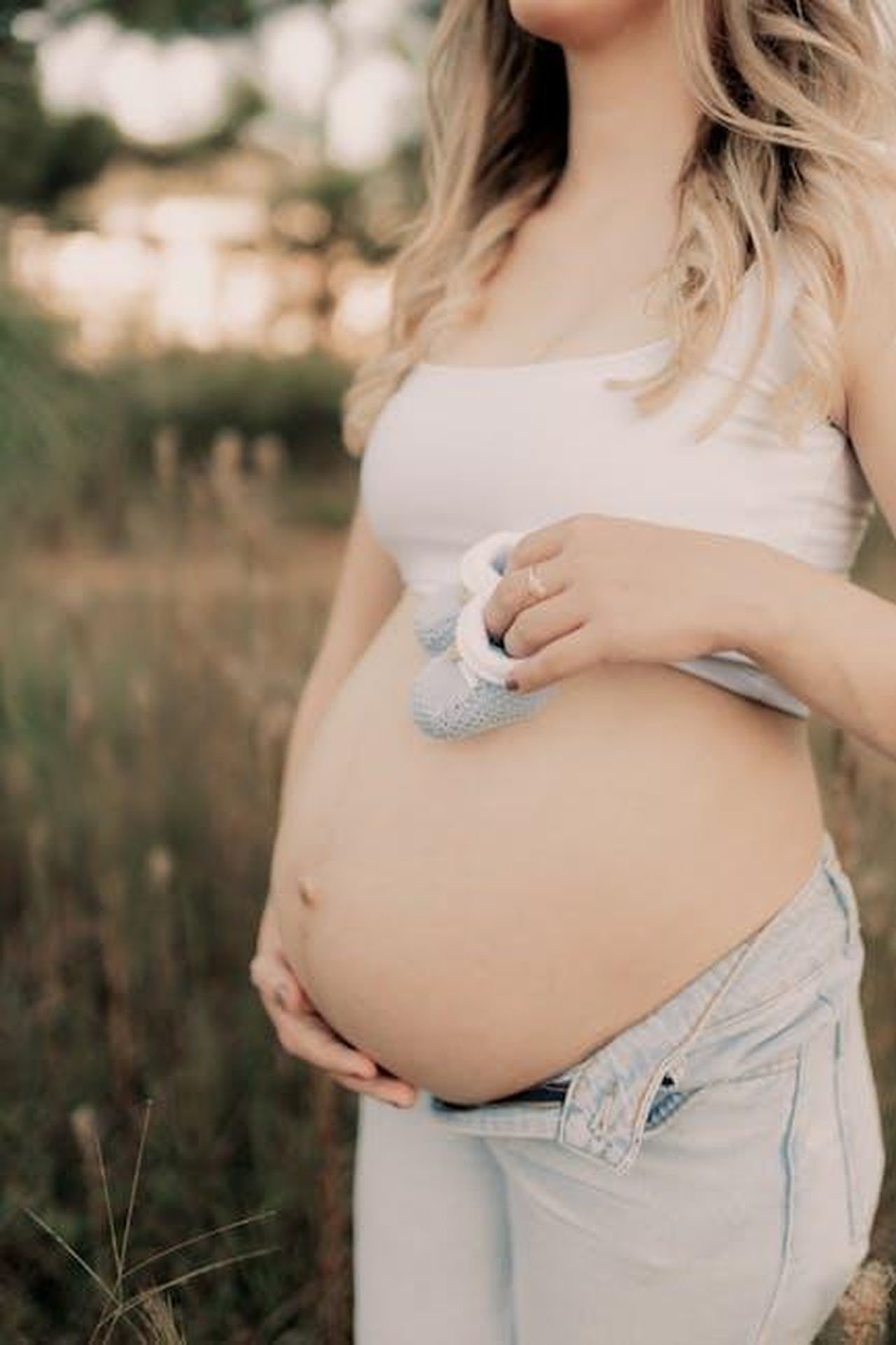 Limportanza_di_esperienze_normali_per_i_reali_rNyRI7k3Kf - Confidenze24 Source: Alexander Mass - pexels - Expectant mother holds baby shoes on her belly in a serene outdoor setting.