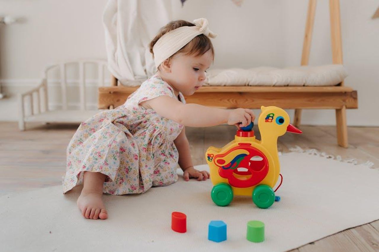 Limportanza_di_lasciare_i_bambini_divertirsi_infycpIIkq - Confidenze24 Source: Polesie Toys - pexels - Cute baby girl in a floral dress playing with a colorful duck toy indoors.