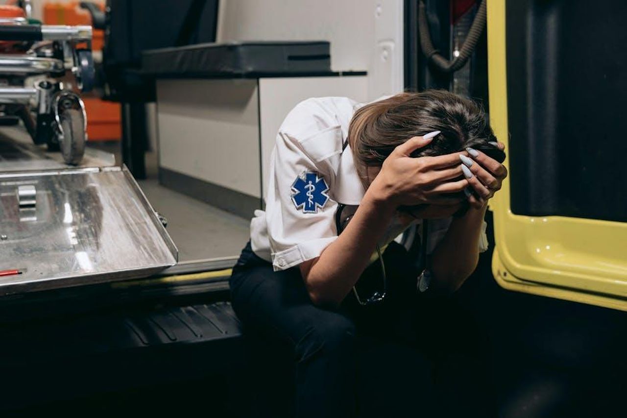 Lincidente_e_il_coma_lDWOhPbBQT - Confidenze24 Source: Mikhail Nilov - pexels - EMT in distress sitting inside an ambulance, head in hands signifying stress and exhaustion.