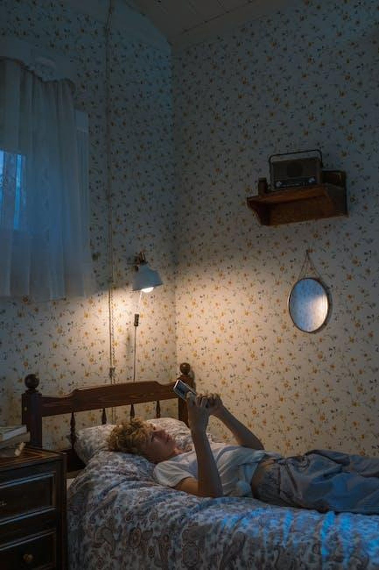 Lotti_con_privacy_e_confini_mWBGm8v6Pe - Confidenze24 Source: Ron Lach - pexels - A teenager lies on a bed using a smartphone in a cozy, vintage-styled bedroom setting.