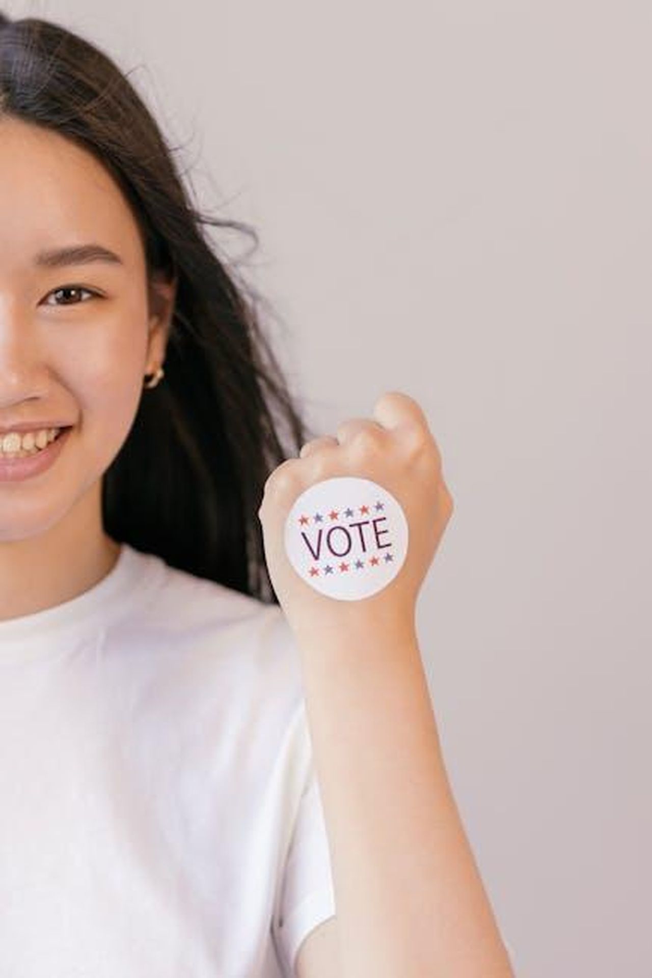 Louis_Church__una_forza_positiva_nella_vita_di_Tushaan_KjkOKnFkUo - Confidenze24 Source: Mikhail Nilov - pexels - A young woman smiling as she holds a 'Vote' sticker, promoting election participation.