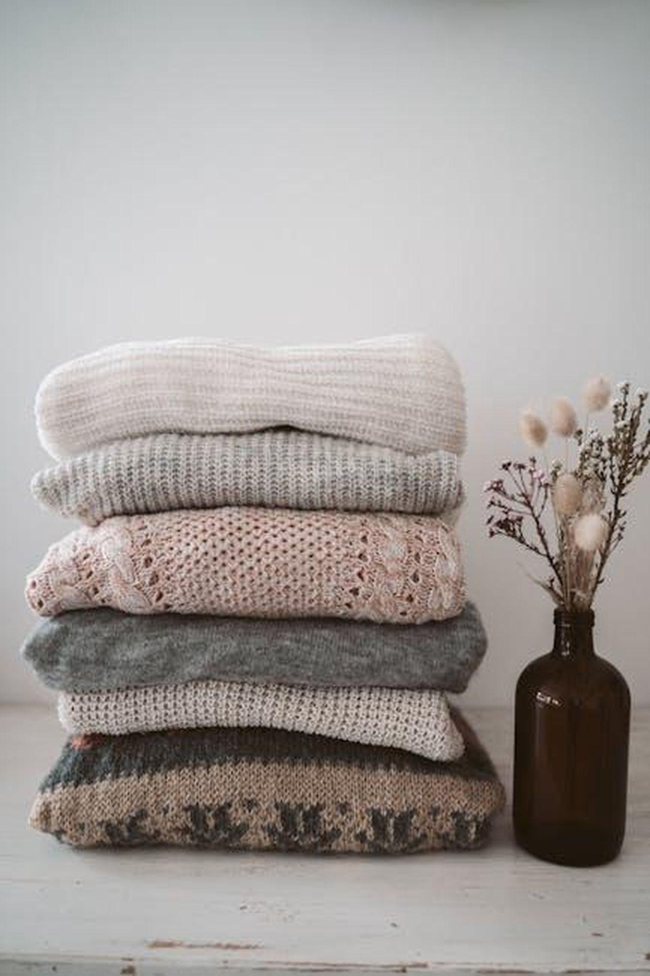 Maglioni_e_abbigliamento_in_cashmere_nmGJBCQLcV - Confidenze24 Source: Taryn Elliott - pexels - A neat stack of cozy knitted sweaters beside a vase with dried flowers, ideal for winter fashion.