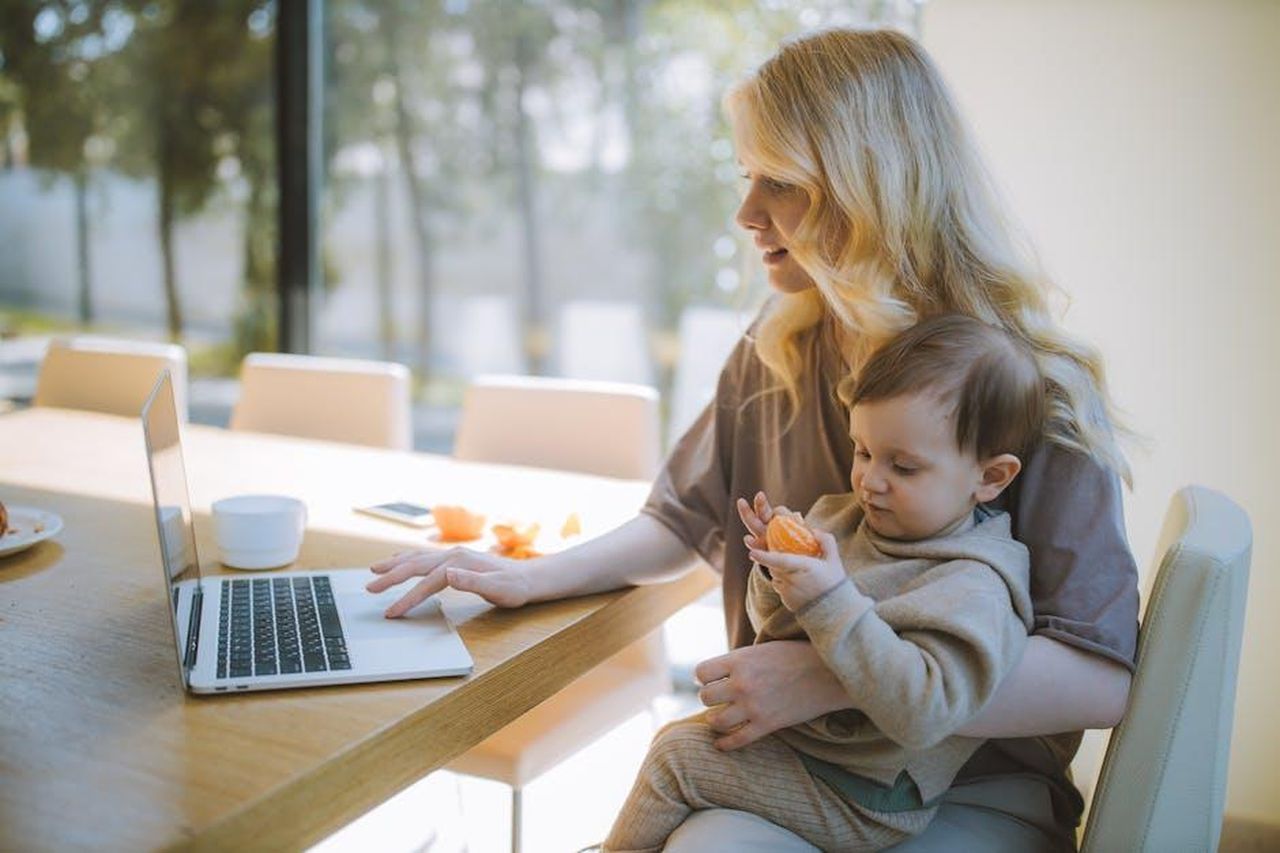 Maternit_lavorativa_Mq76c321Em - Confidenze24 Source: Anastasia Shuraeva - pexels - A mother works on a laptop at home while holding her baby, showcasing remote working and parenting.