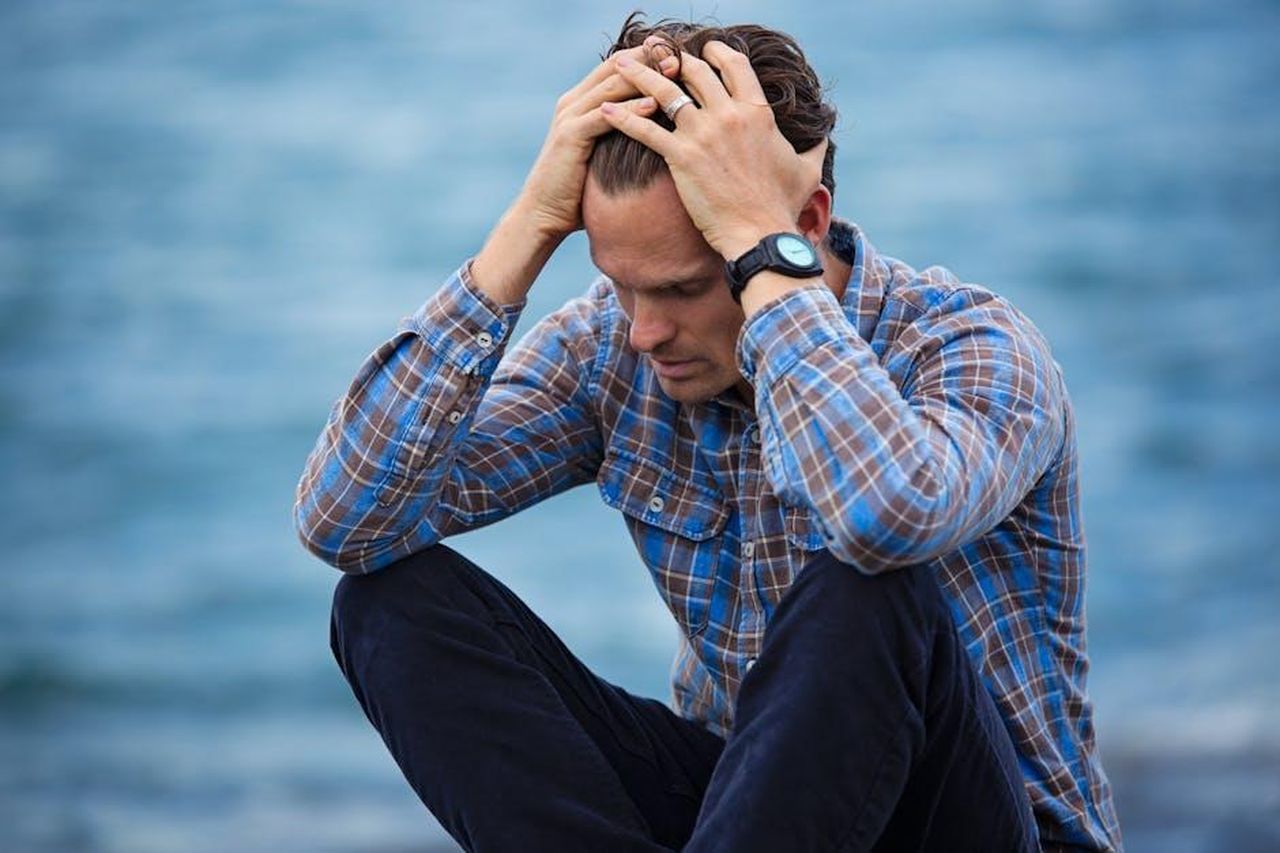 Minacce_di_dimissioni_epCk3utABF - Confidenze24 Source: Nathan Cowley - pexels - A man in a plaid shirt sits by the water looking distressed, symbolizing stress.