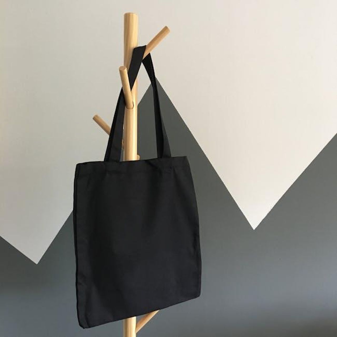 Mini_Ella_Bio_Tote_stile_e_sostenibilit_wwHYkFrRFA - Confidenze24 Source: Stephanie Ho - pexels - Simple and elegant black canvas tote bag hanging on a wooden rack, perfect for eco-friendly shopping.