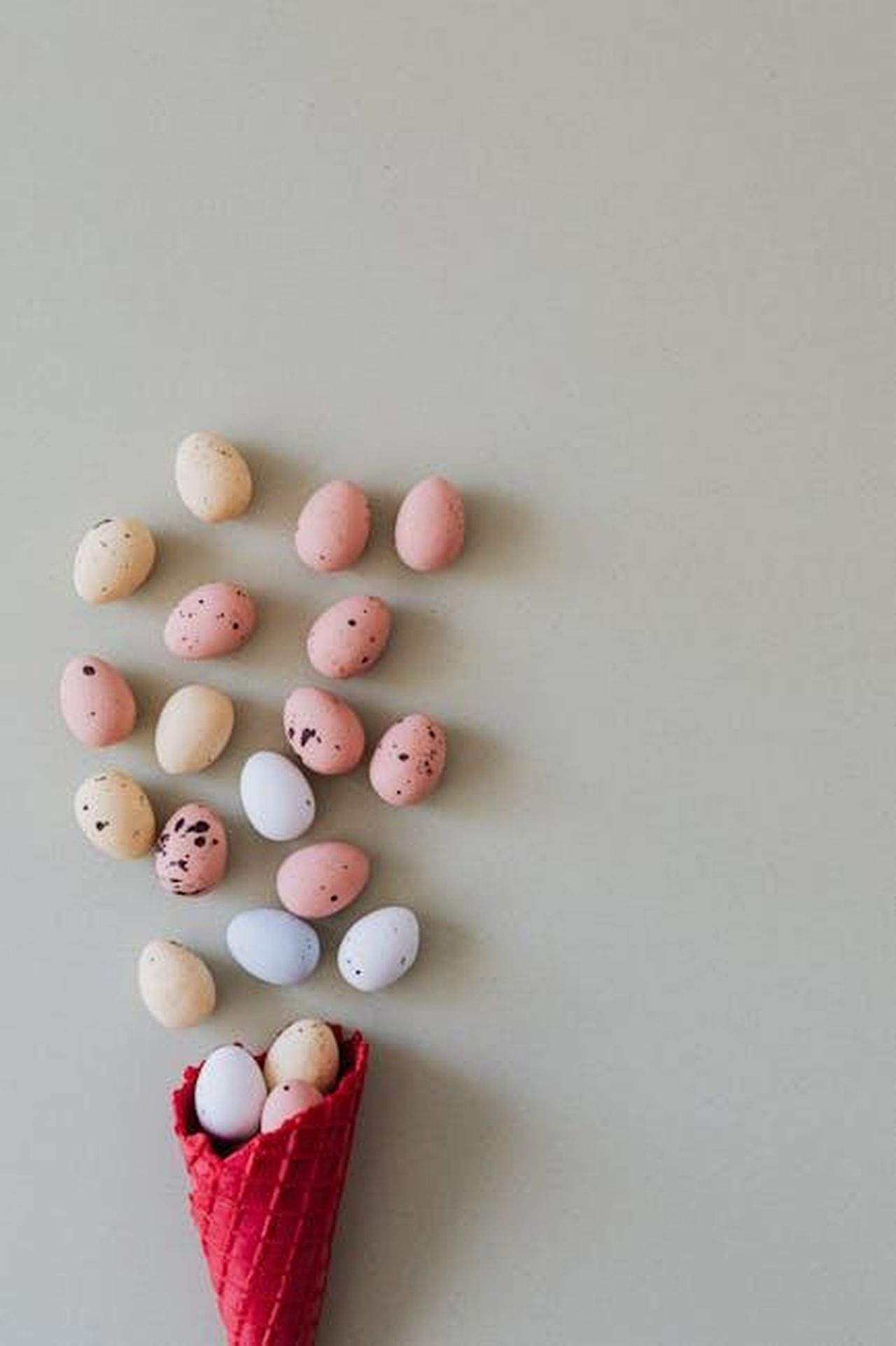 Mini_Waffle_Maker_PEEPS_x_Dash_Bunny_XKu5psOGkI - Confidenze24 Source: Photo By: Kaboompics.com - pexels - A creative arrangement of pastel Easter eggs spilling from a red waffle cone against a neutral background.