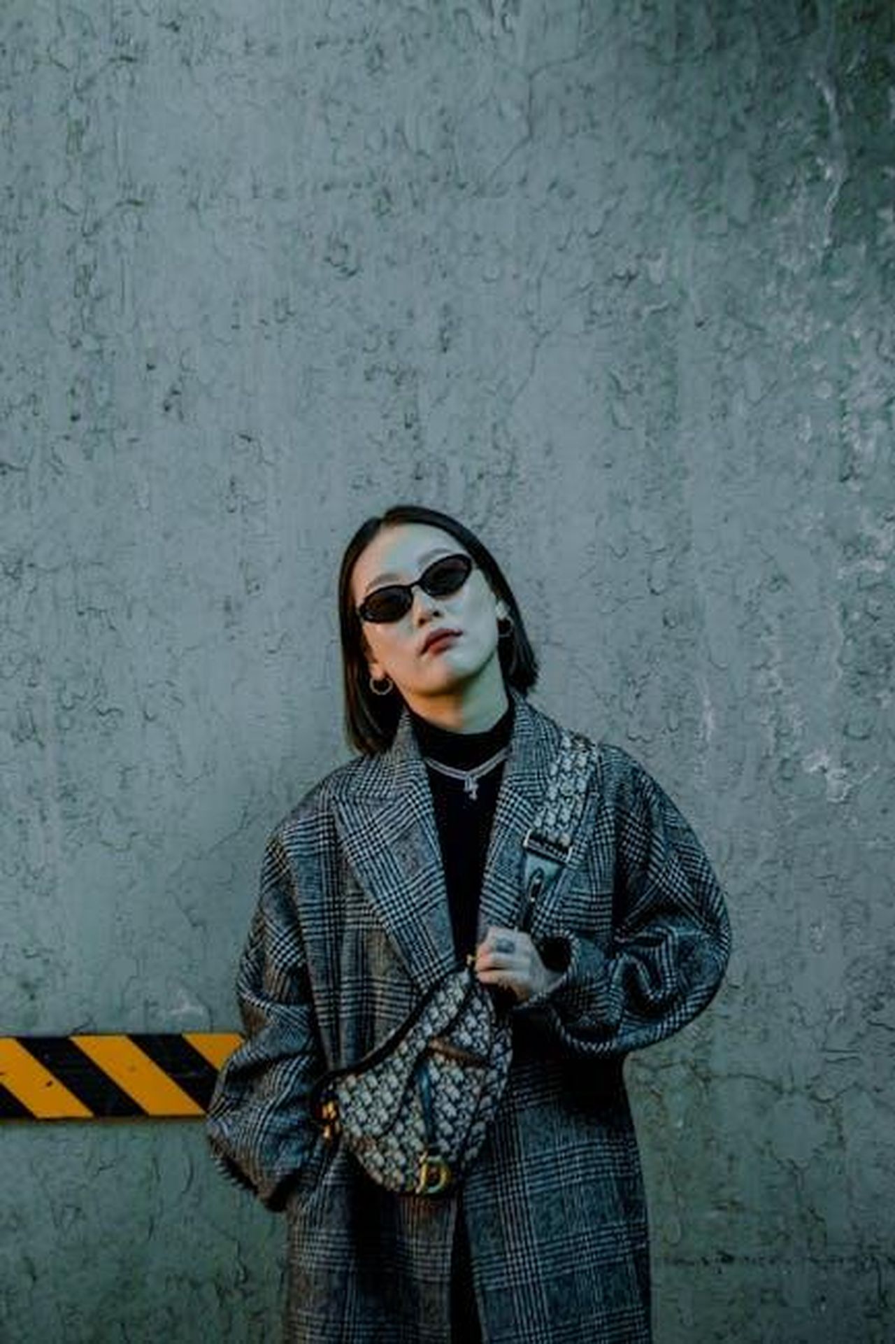 Minnie_Belt_Bag_praticit_e_stile_qMPQoUtGsi - Confidenze24 Source: mikoto.raw Photographer - pexels - Edgy portrait of a fashionable woman in sunglasses and a chic coat against an urban backdrop.