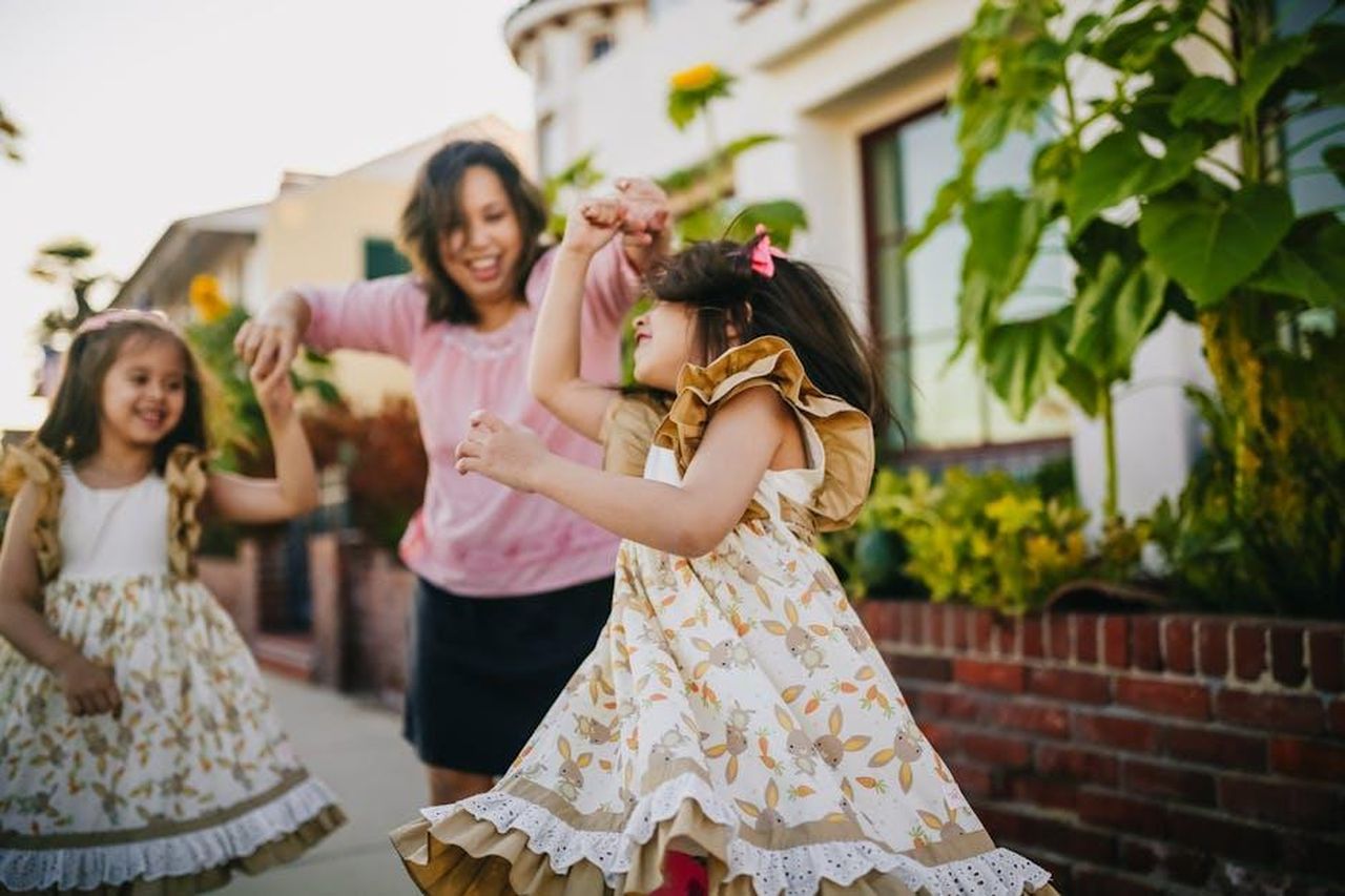 Miranda_Hope__una_mamma_single_di_due_bambini_KC9NmIZzBy - Confidenze24 Source: RDNE Stock project - pexels - A mother dances with her twin daughters in a lively outdoor setting, enjoying a sunny day.