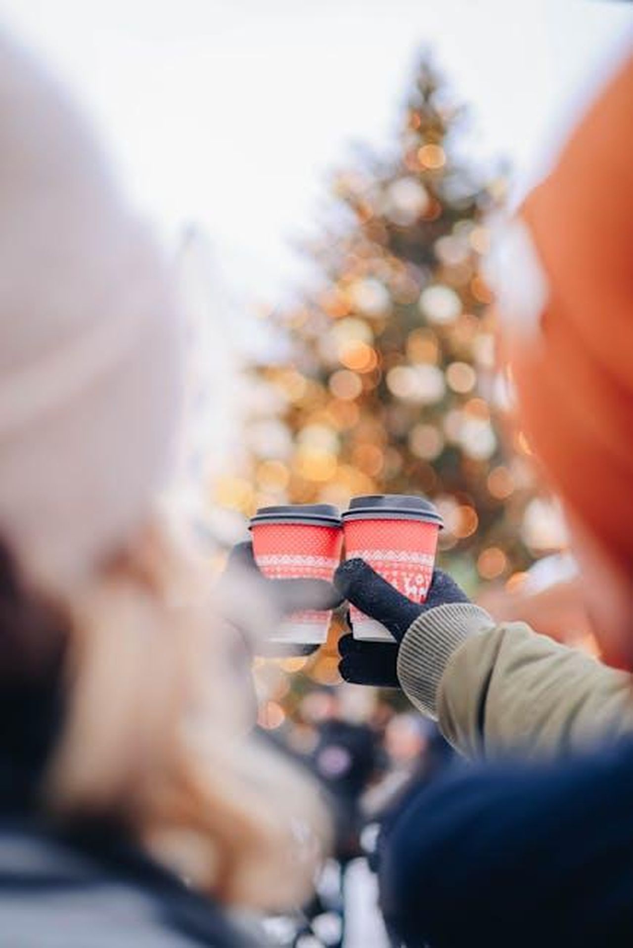 Source: Valeria Boltneva - pexels - Couple holding festive coffee cups near a decorated Christmas tree outdoors.