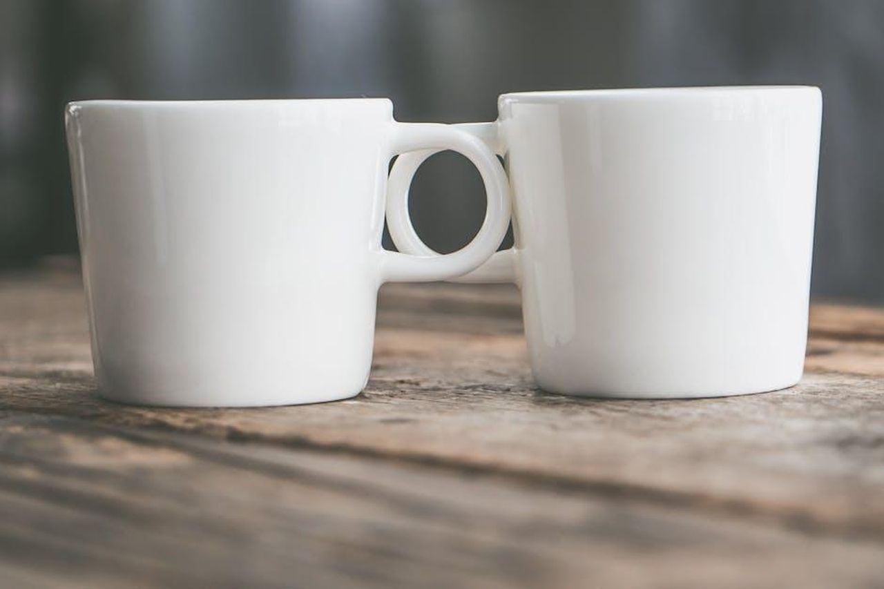 Momenti_significativi_dal_1983_al_2025_ZJrxqwAgEA - Confidenze24 Source: Jessica Lewis 🦋 thepaintedsquare - pexels - Two connected white ceramic cups on a rustic wooden surface, showcasing depth of field.