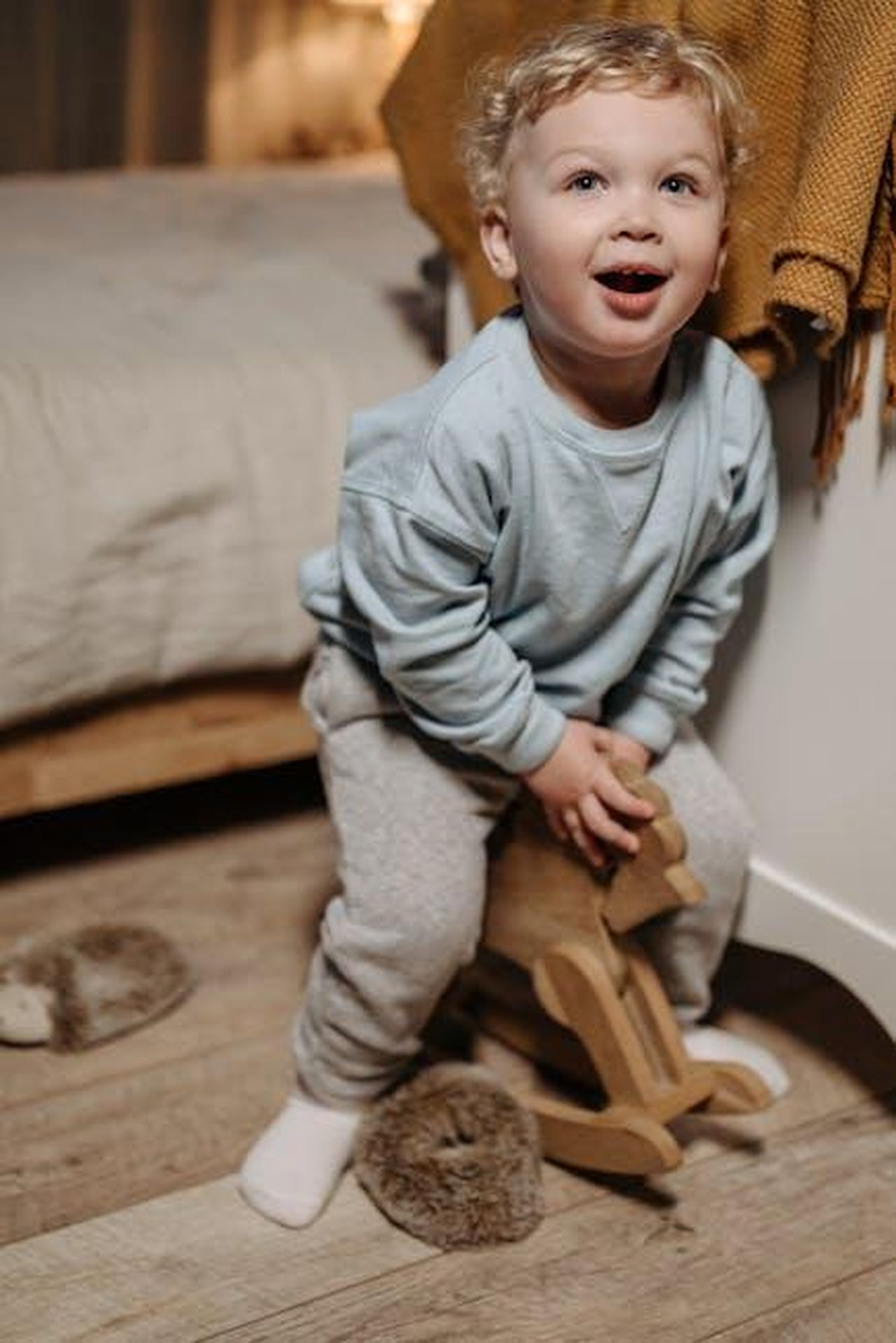 Momenti_speciali_in_famiglia_GLv8ThA9b3 - Confidenze24 Source: Pavel Danilyuk - pexels - A cheerful toddler in a blue sweater sits on a wooden rocking horse indoors.