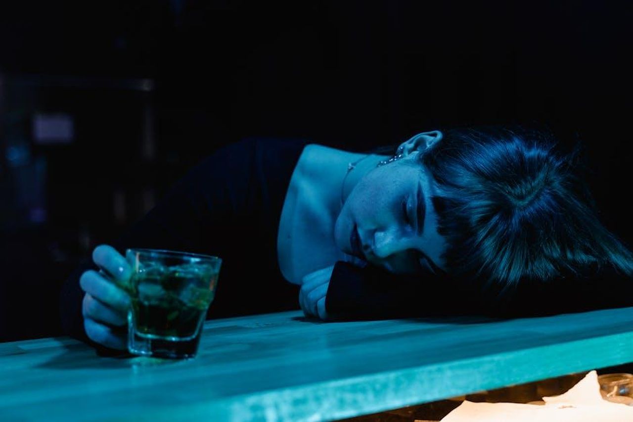 Musica_e_affetto_un_legame_speciale_euFp8autkL - Confidenze24 Source: MART PRODUCTION - pexels - A woman resting her head on a bar table while holding a drink, in a moody, dimly-lit nightclub setting.