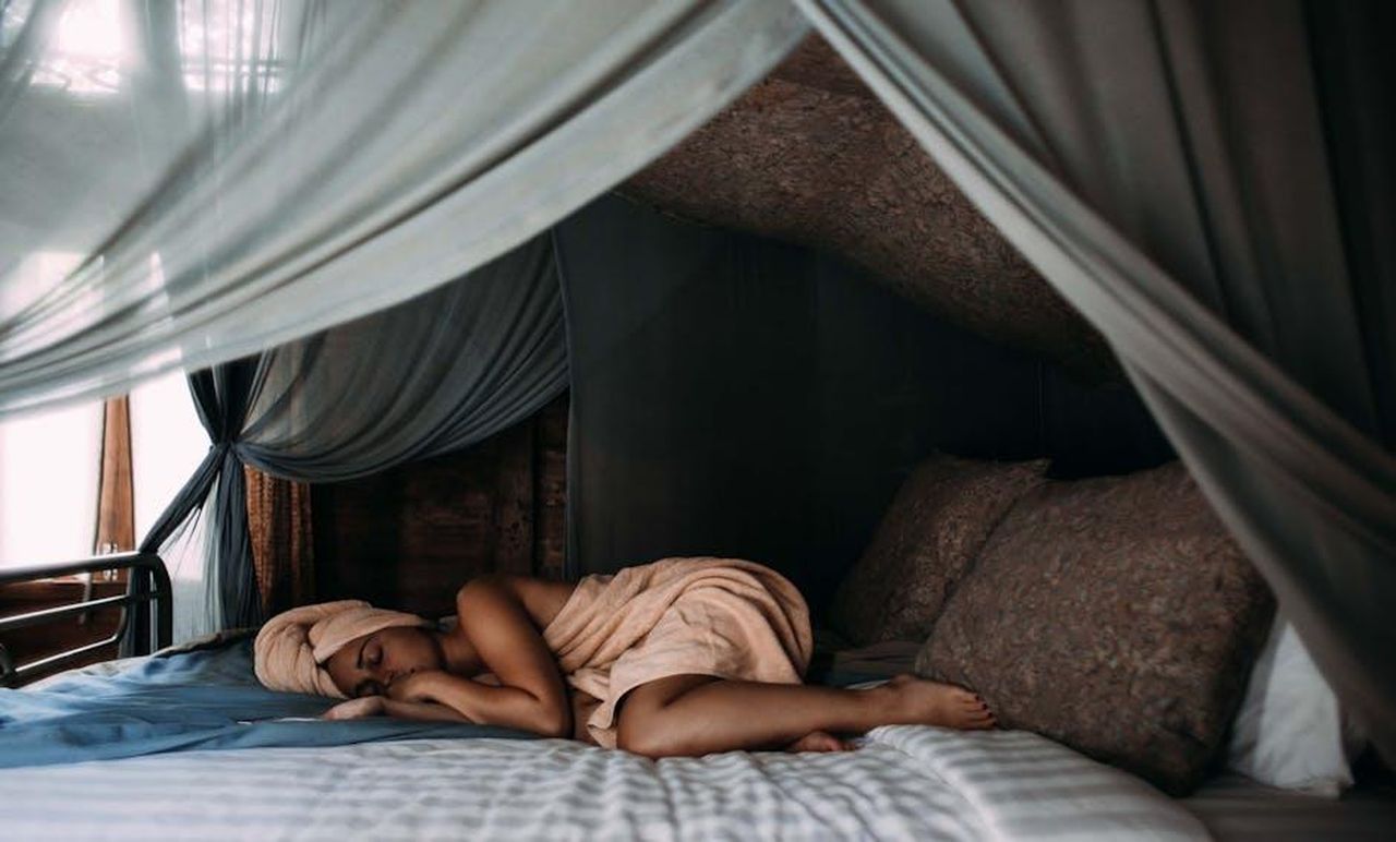 Non_Dimenticare_di_Dare_Priorit_a_un_Sonno_Ottimale_RLbuqPmlo1 - Confidenze24 Source: Rachel Claire - pexels - A woman rests peacefully on a cozy bed with sheer canopy curtains, creating a tranquil indoor retreat.