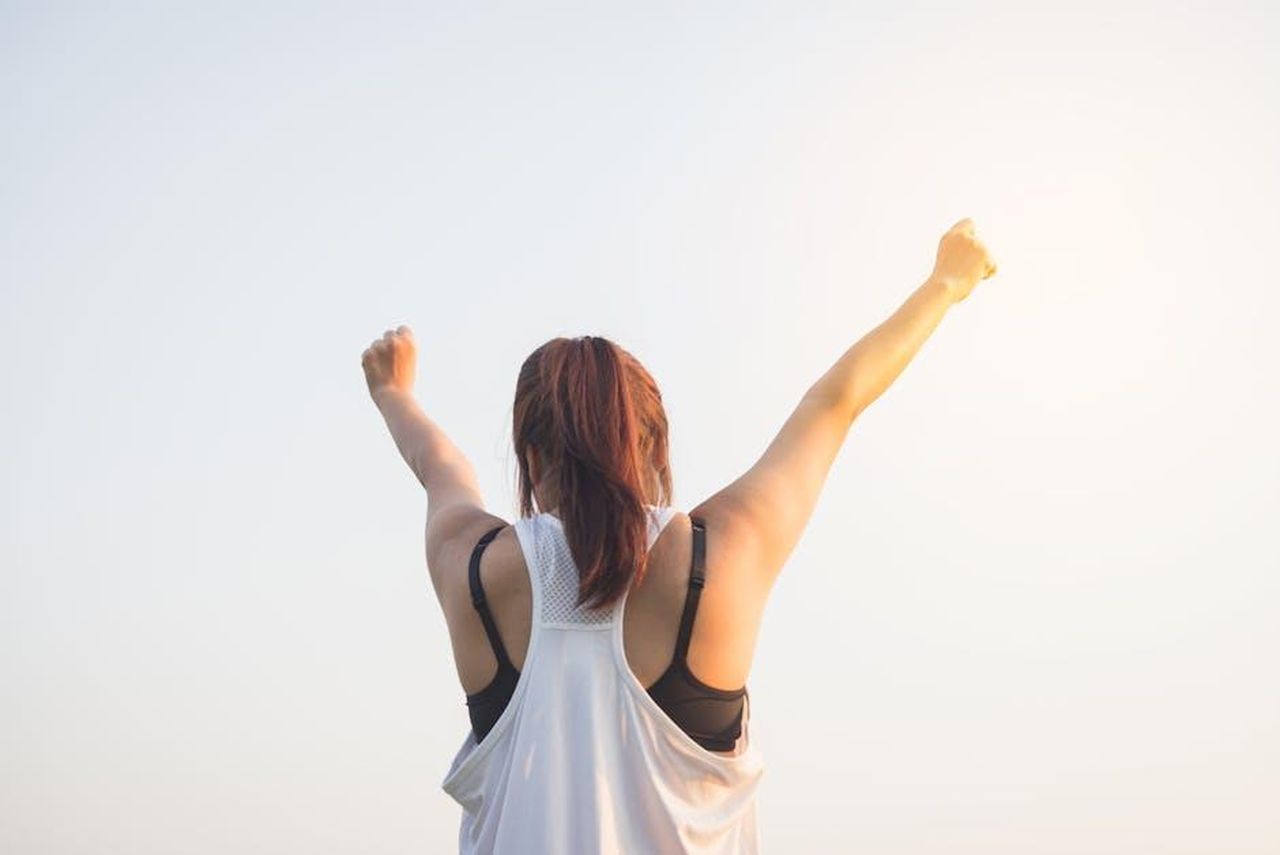 Non_vuole_sentirsi_sotto_pressione_per_fare_benessere_8PR8pMnch6 - Confidenze24 Source: Tirachard Kumtanom - pexels - A woman celebrates success with arms raised in a bright outdoor setting.