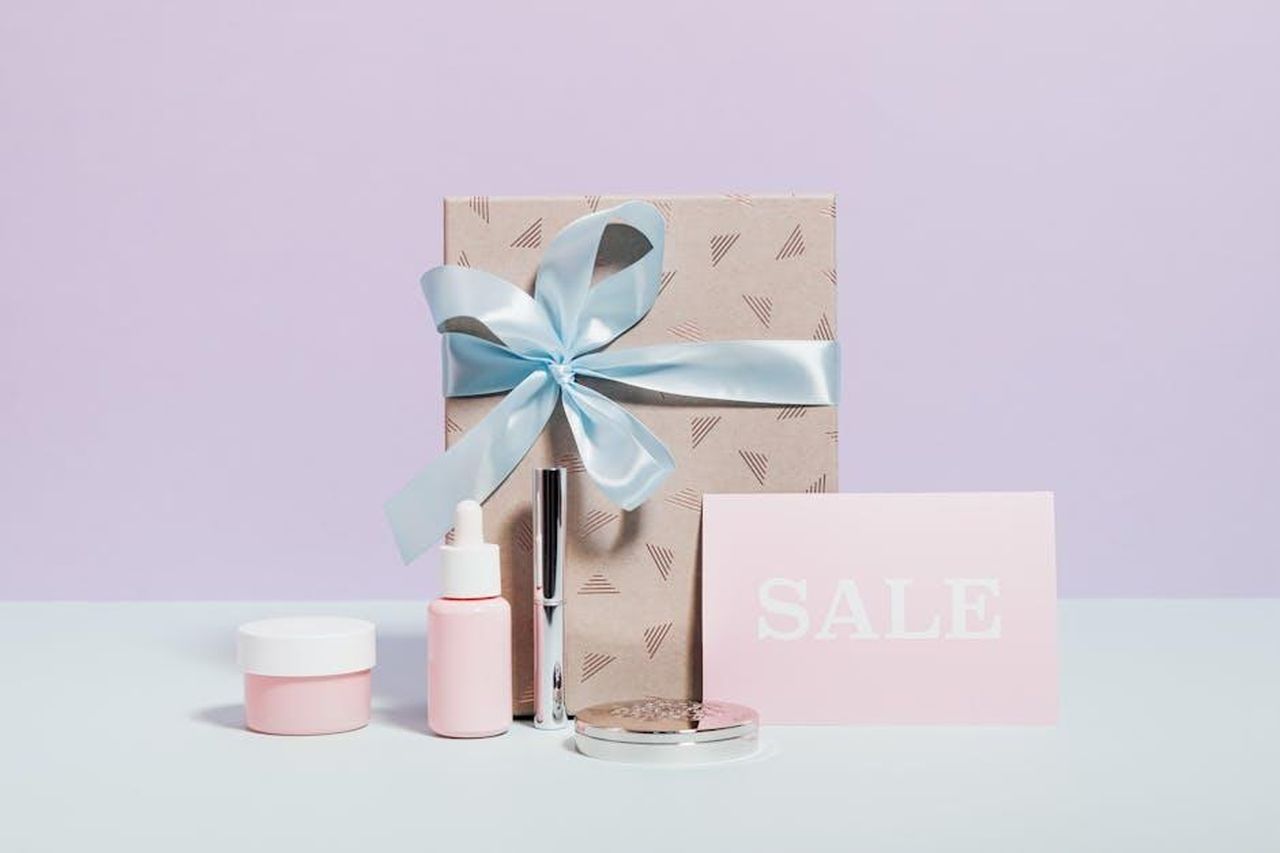 Offerte_attuali_su_I_DEW_CARE_Tap_Secret_2jrhZGt1gW - Confidenze24 Source: Photo By: Kaboompics.com - pexels - Stylish flat lay of beauty products and a gift with sale signage, perfect for promotions.