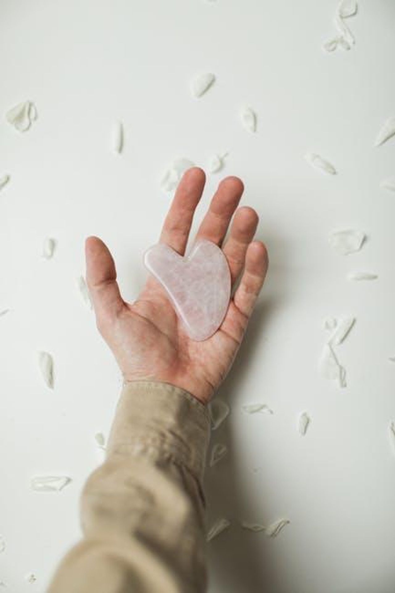 Pacifica_e_limpegno_per_la_bellezza_pulita_KbGTvK6aB3 - Confidenze24 Source: Cup of Couple - pexels - A hand holds a rose quartz gua sha amidst scattered petals, symbolizing self-care and relaxation.