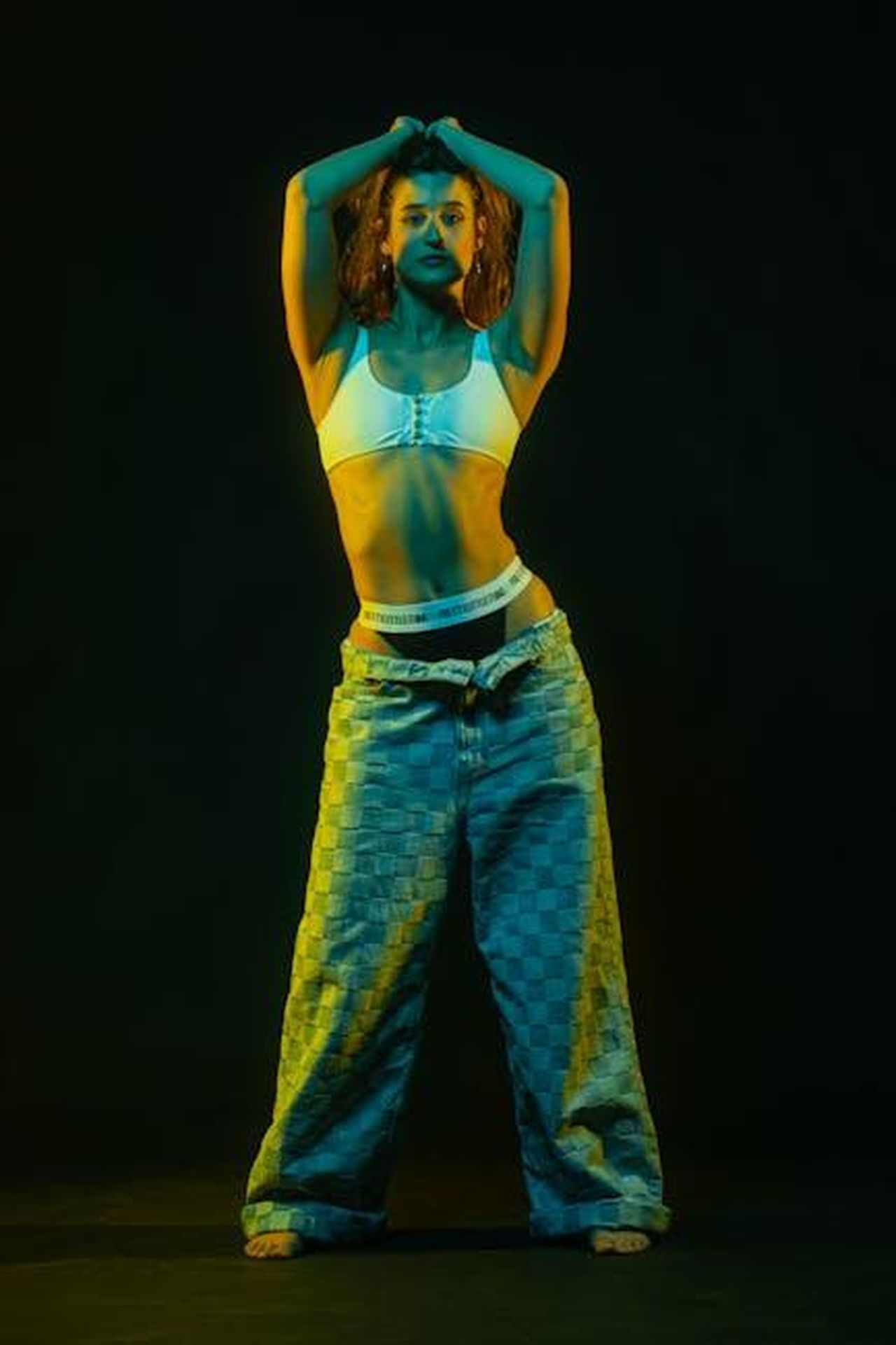 Pantaloni_larghi_plissettati_in_crepe_stretch_fiGX3ALwbf - Confidenze24 Source: Moisés Fonseca - pexels - Artistic studio portrait of a woman in plaid pants with vibrant blue and yellow lighting.