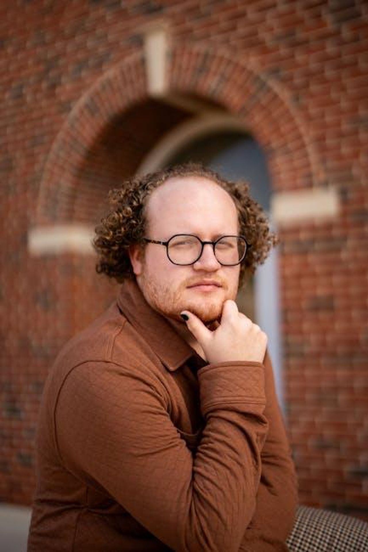 Perch_Amziah__il_progetto_giusto_ND06X7yCIx - Confidenze24 Source: Jamie Kimball - pexels - A thoughtful man poses beside a brick archway, capturing a modern, warm vibe.