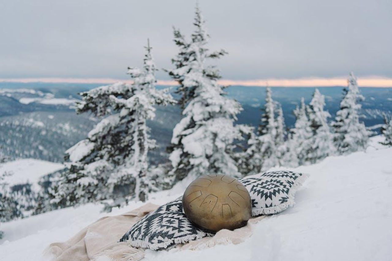 Perch_Greg__tornato_nella_stagione_3_IIdCQlpNru - Confidenze24 Source: Mikhail Nilov - pexels - Snowy mountain landscape with a meditation setup including a metallic drum and patterned cushion, evoking tranquility.