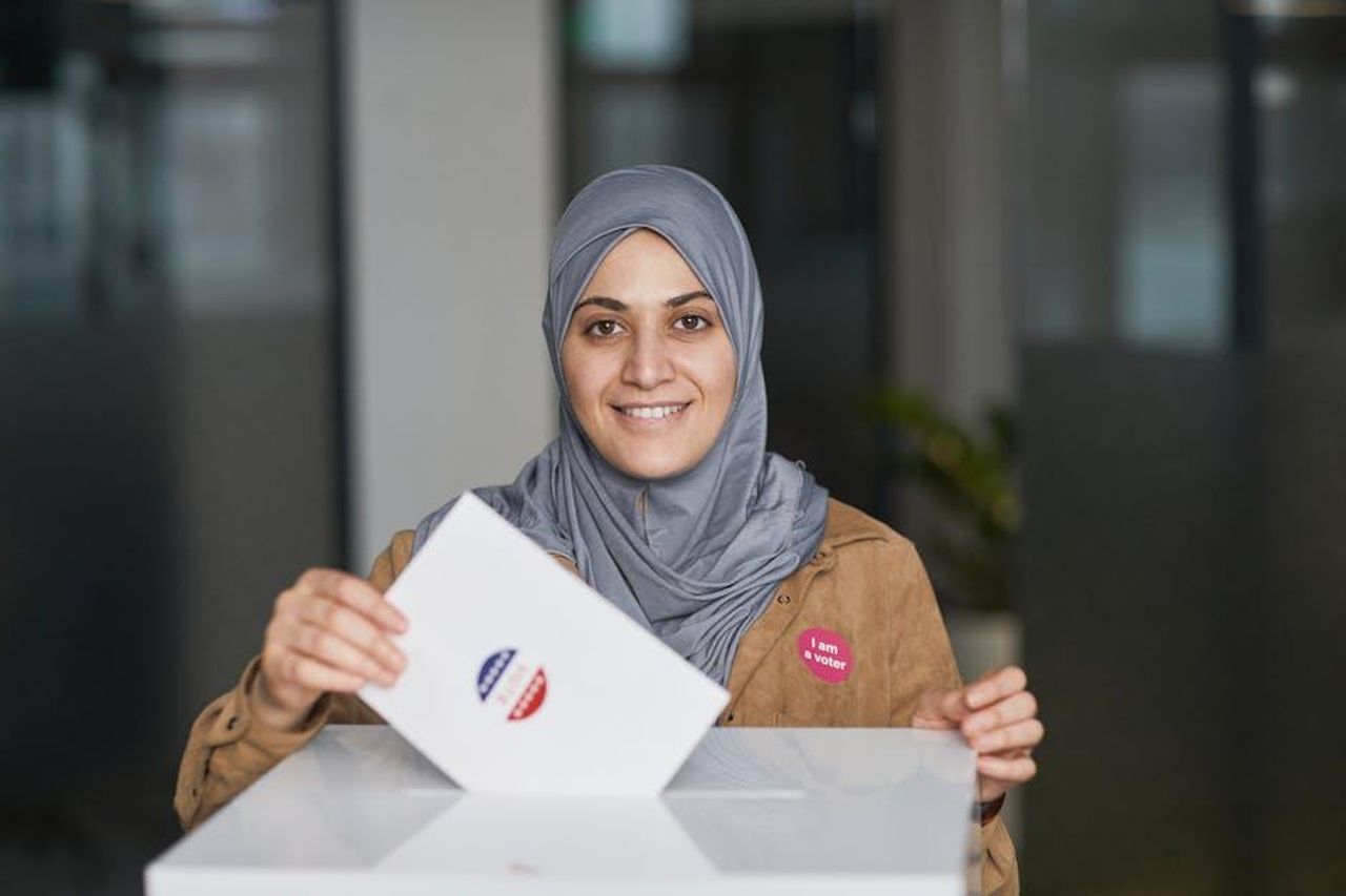 Perch_James_Bailey__stato_ricastato_GxIRFYebtD - Confidenze24 Source: Edmond Dantès - pexels - A smiling woman wearing a hijab casts her vote at a polling station indoors.