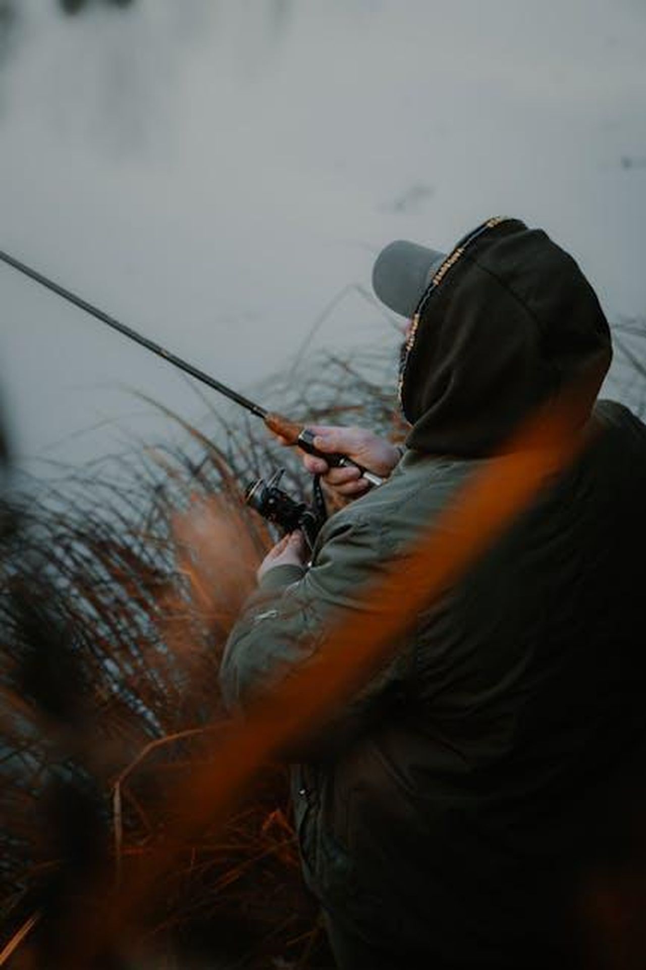 Perch_James_Bailey__stato_ricastato_oeAKvbzqzu - Confidenze24 Source: Cedé Joey - pexels - A man in a hoodie fishes by a calm lake surrounded by autumn foliage.