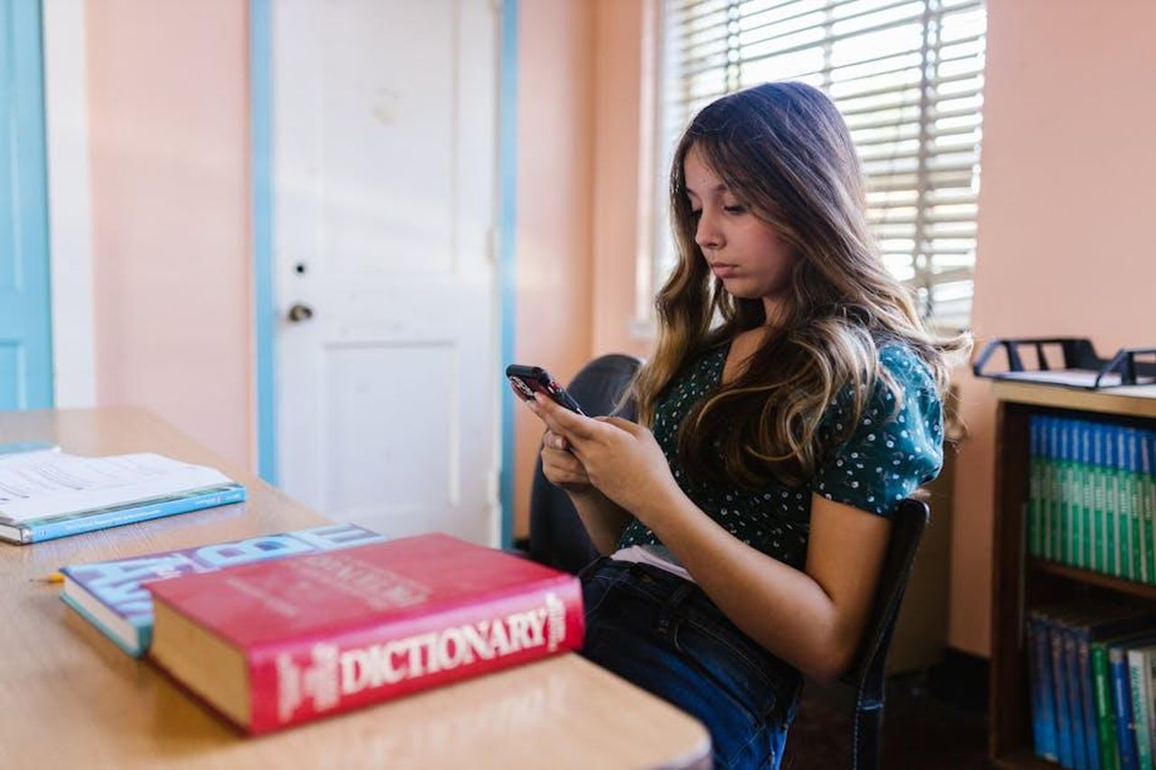 Perch_la_privacy_del_mio_teenager__cos_importante_NvcHAtR3iU - Confidenze24 Source: RDNE Stock project - pexels - A teenage girl sits in a classroom, focused on her smartphone among books and educational materials.